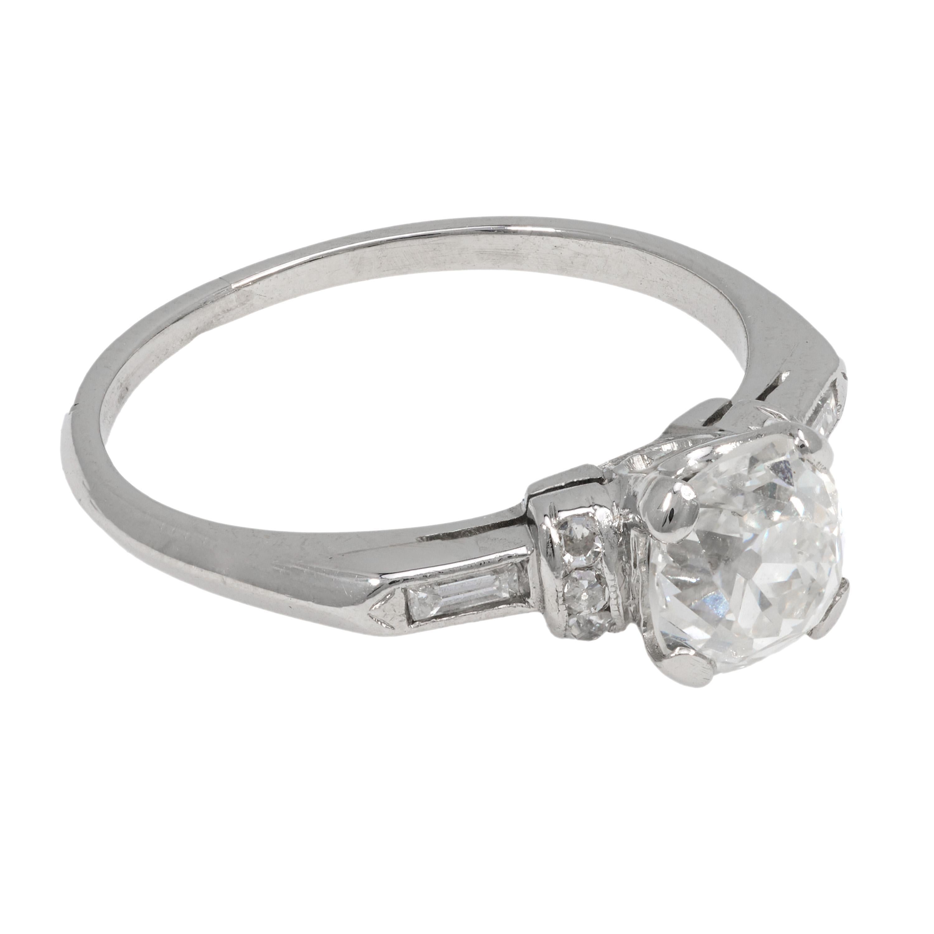 This Art Deco platinum engagement ring centers a 1.23 carat GIA-certified old mine cut diamond, surrounded by eight delicately set baguette and single cut diamonds. Crafted in the 1930s, the setting's geometric elegance and vintage charm embody