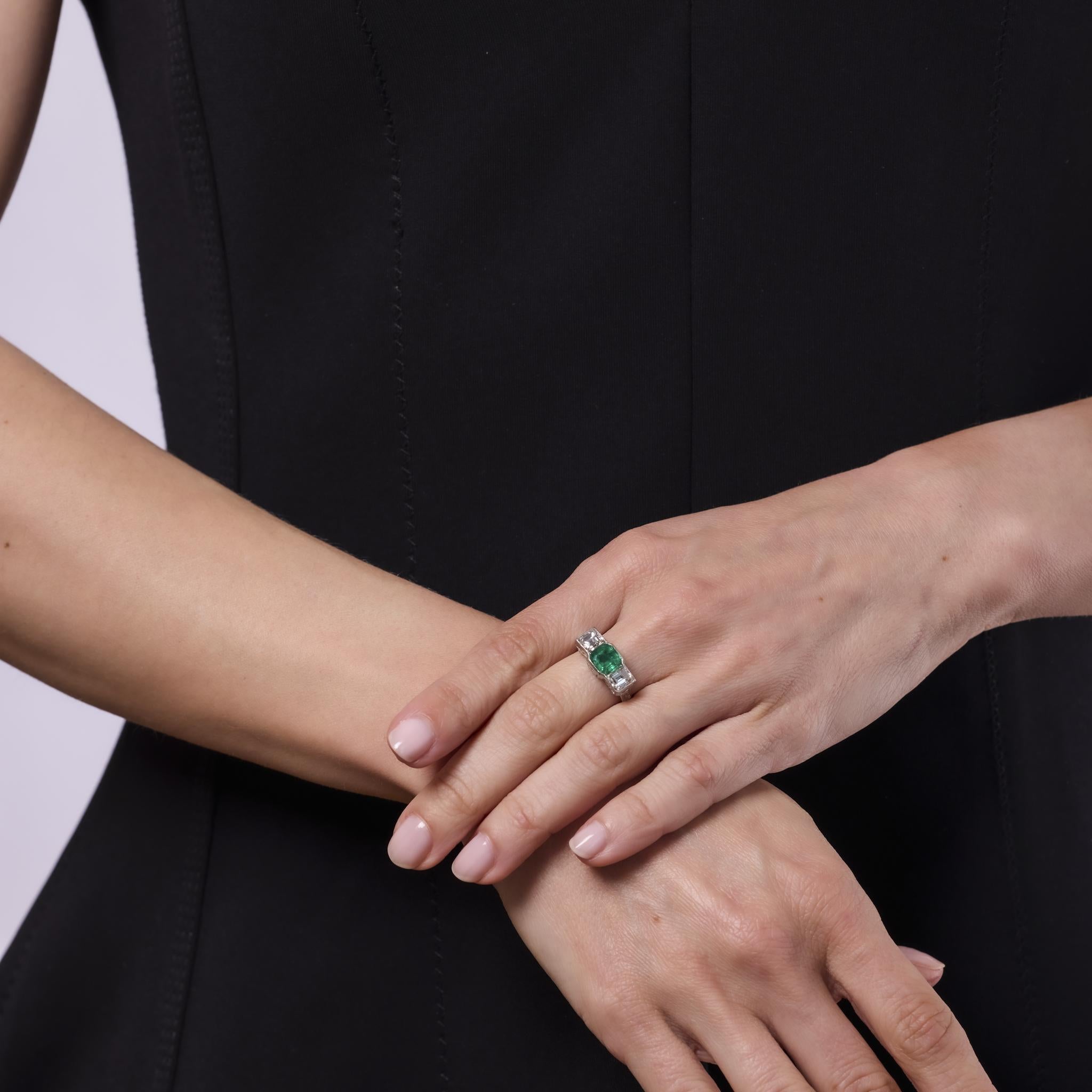 This captivating Art Deco platinum ring showcases a 1.40 carat Colombian emerald with vivid green hues, certified by GIA. Flanked by an architectural mix of carré, trapezoid, and baguette cut diamonds, its bold 1930s design exudes refined glamour