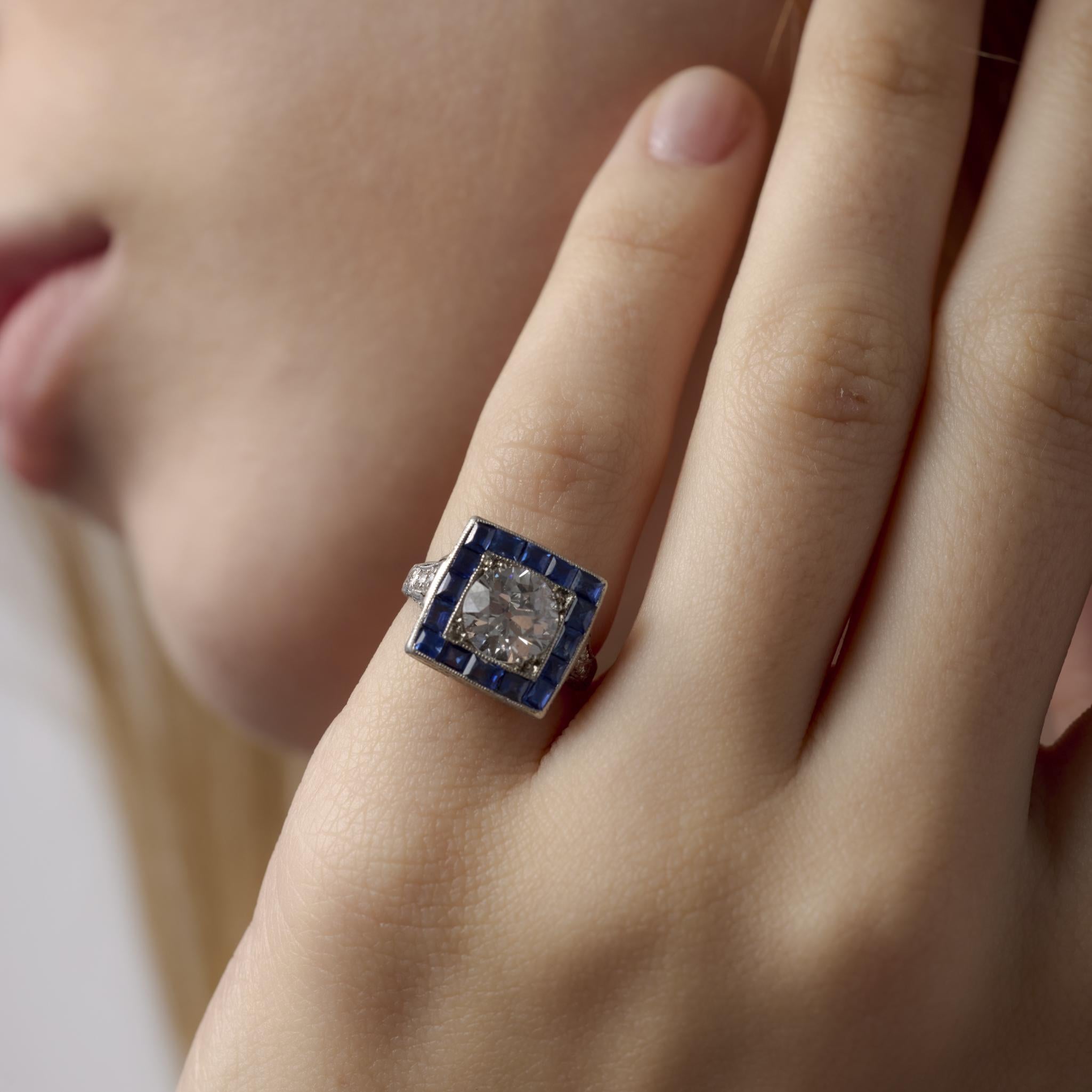 Cette exquise bague Art déco des années 1930 éblouit par son diamant de taille européenne ancienne de 1,53 carat certifié par la GIA, entouré d'un halo vibrant de saphirs bleus taillés en calibre et de diamants d'accentuation étincelants, le tout