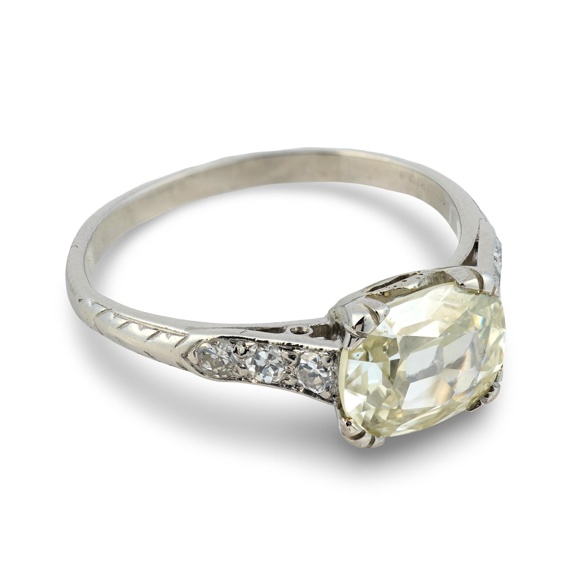 Este anillo de compromiso Art Decó exhibe un diamante alargado de talla mina antigua cuyas facetas suaves y abiertas brillan con carácter vintage. El tono cálido de la piedra central está realzado por seis brillantes diamantes de talla europea