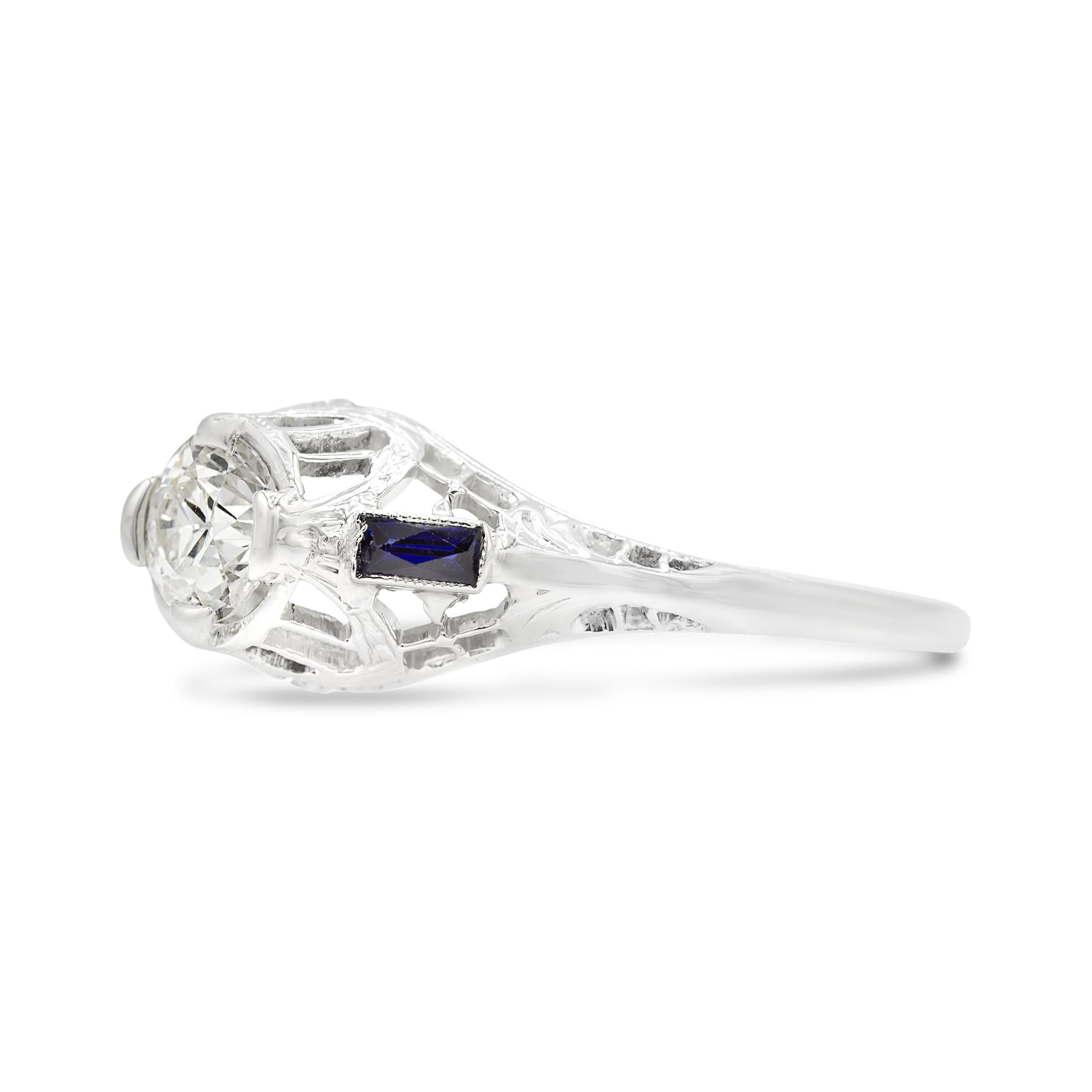 This charming Art Deco engagement ring is your vintage partner in time. The center bezel-set 0.50 ct. old European diamond flashes with chunky facets and a small table, and is flanked by 2 long, calibre sapphire baguettes. Fashioned in white gold,