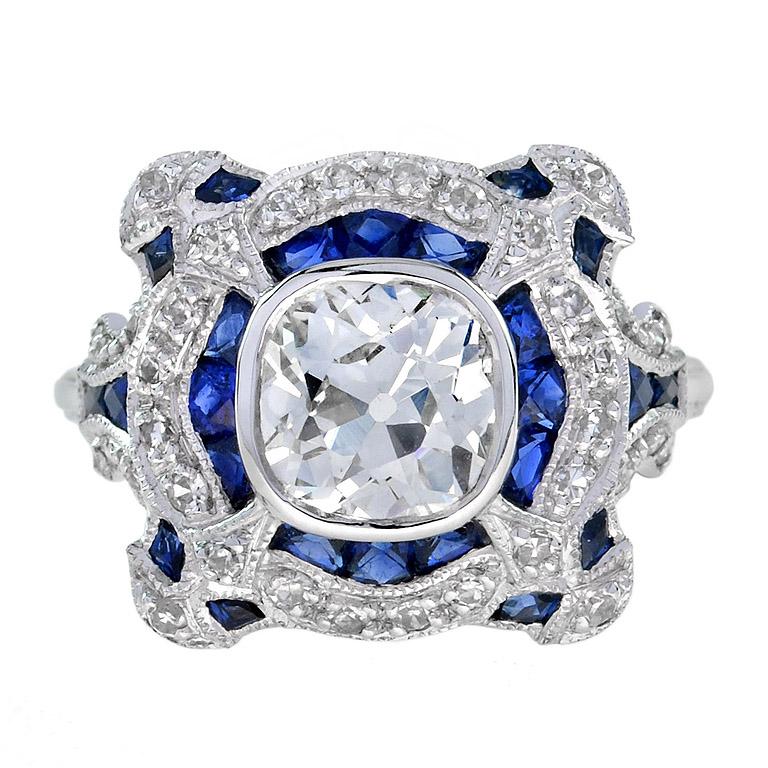 Featured is a beautifully designed Art-Deco style diamond ring setting that has been fitted with a round-shaped ring face top encrusted with blue sapphires and natural diamonds. The centerpiece is an old mine cut diamond graded J in color and VS2 in