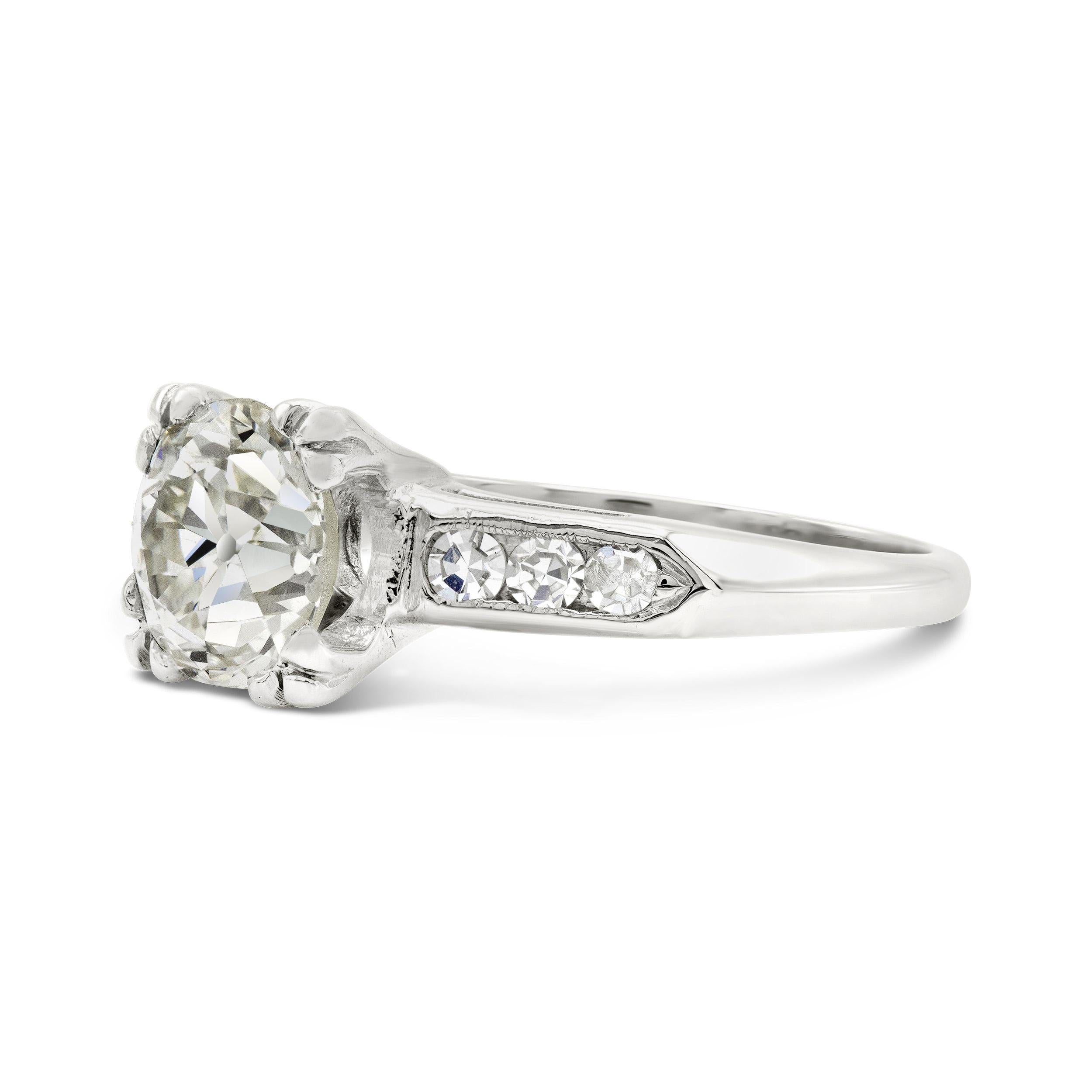 Dieser Verlobungsring ist der Inbegriff des Dekos schlechthin. Ein prächtiger Diamant im alten europäischen Schliff mit offener Kalette und glitzernden Facetten stiehlt ihm die Show. Wir sind von seinem prismatischen Funkeln und den ebenso