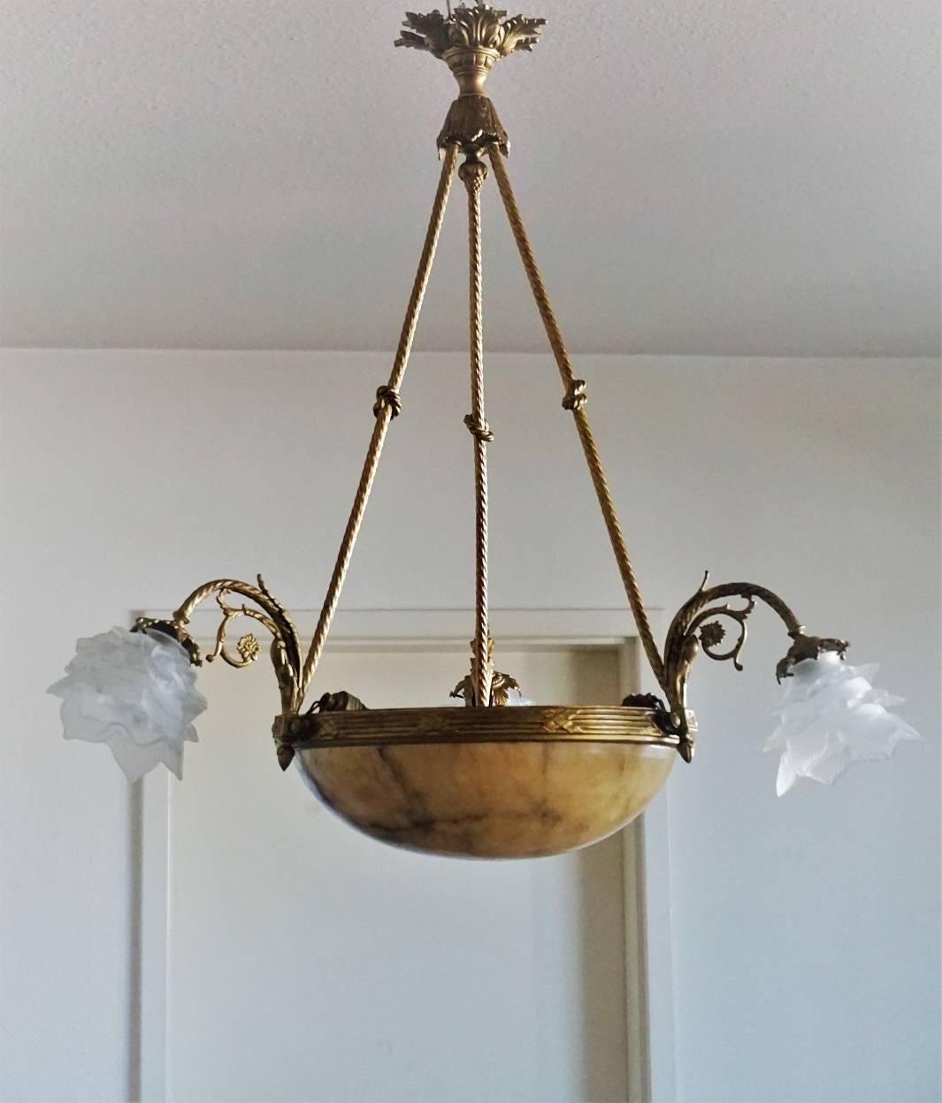 Large French Art Deco gilt bronze chandelier with alabaster bowl shade suspended from three gilt bronze arms with knotted rope shape. Three curved arms richly ornate with frosted glass flower shades, early 20th century.
Number of lights: Six French
