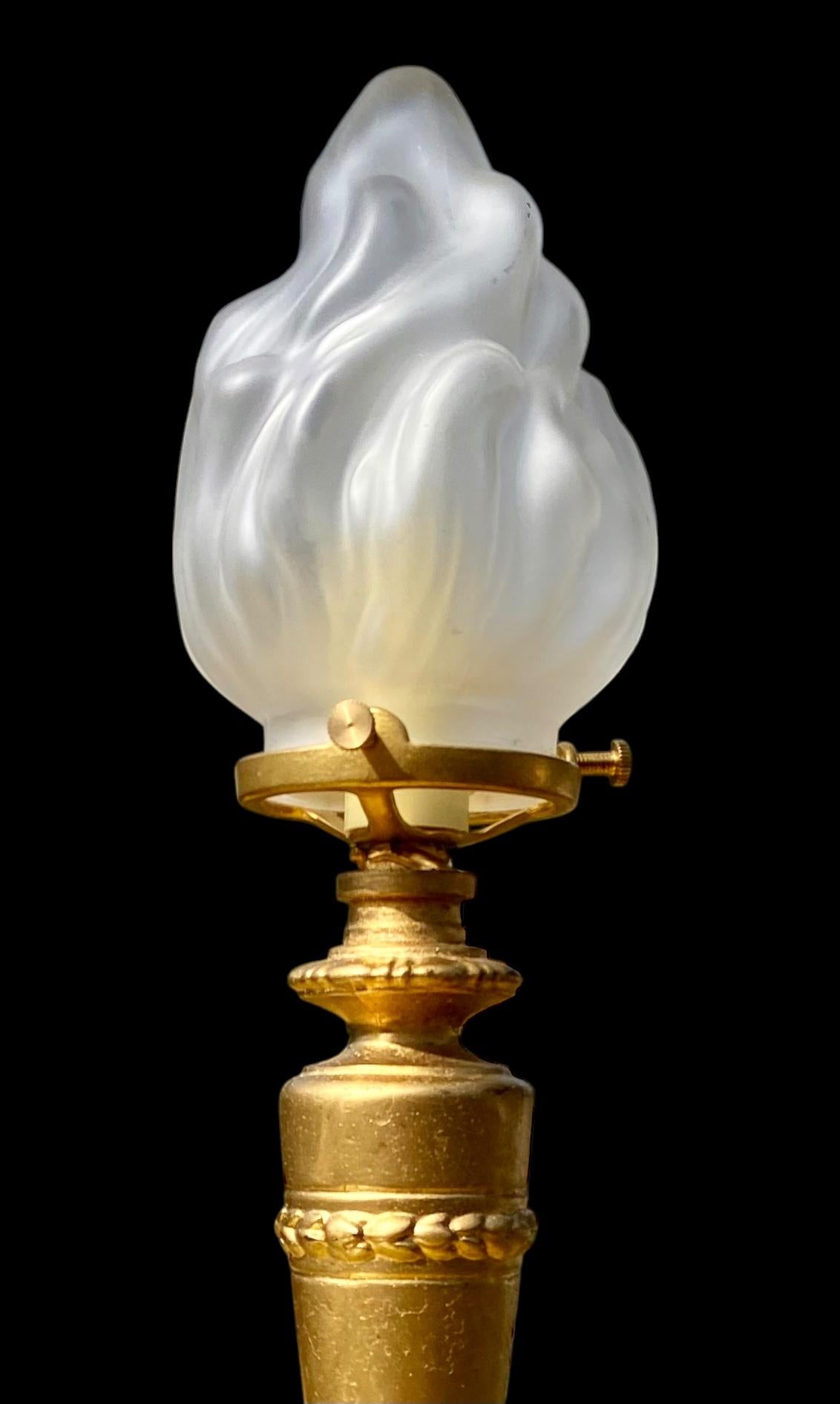 An American Art Deco gilt spelter column table lamp having an onyx disc above a ring of pierced, stylized anthemions and fans ending in a figured marble base. A handsome frosted glass flame shade atop. The cord with an inline switch. 

Quite an