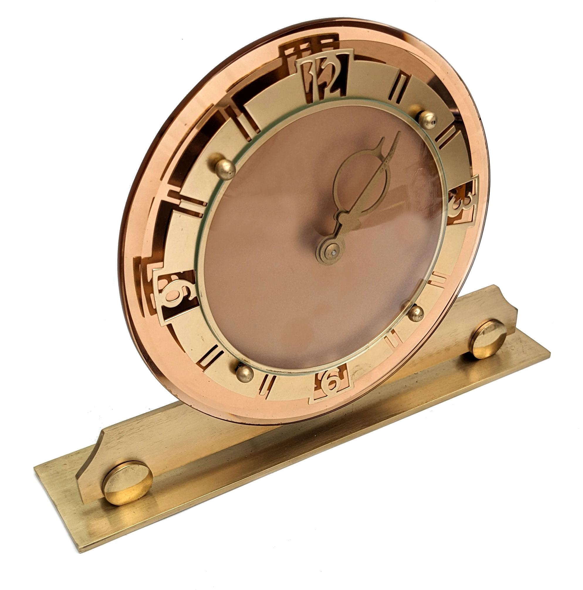 This is a very attractive English Art Deco clock, made circa 1930. It has a eight day wind up movement. The base is brass, the bezel is also brass with gold tone finish. The backing glass is peach-coloured mirror . In superb condition. Full working