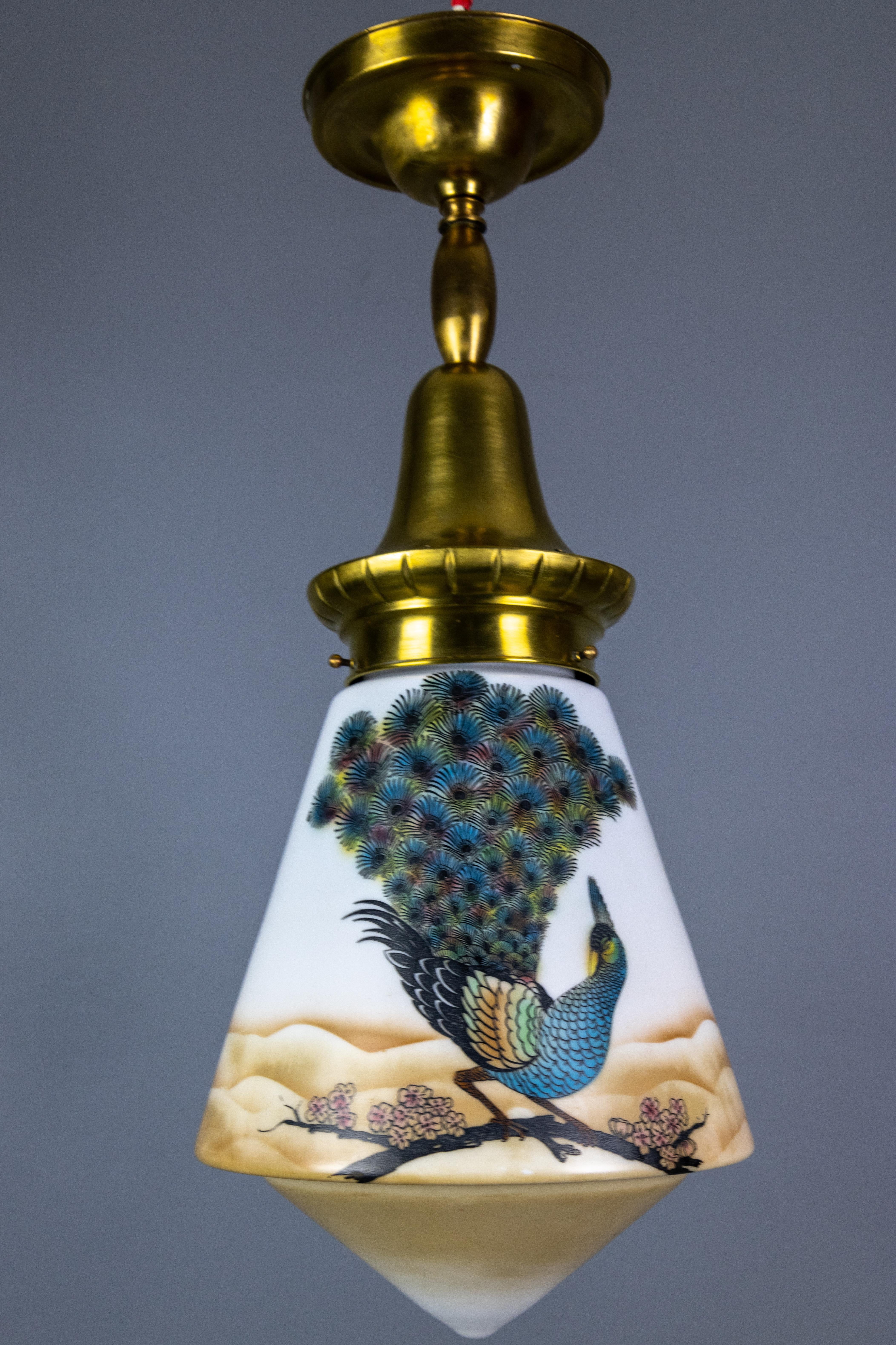 An Art Deco glass and brass pendant light with bird paintings, France, 1930s.
This delightful ceiling light features a beautifully shaped glass lampshade with colorful birds - peacocks on a blossoming Sakura branch. The glass lampshade hangs from a