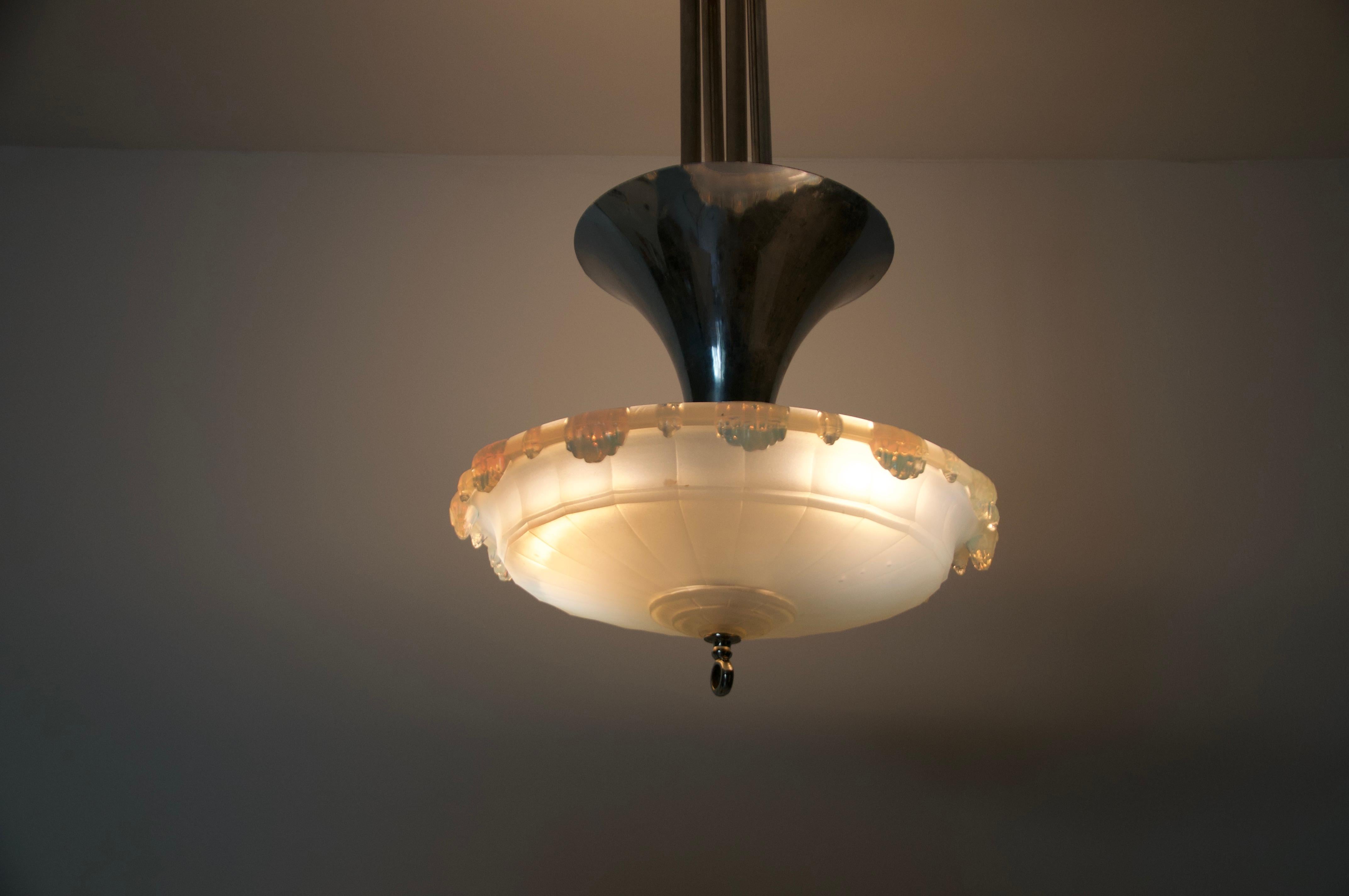 Esta llamativa lámpara colgante Art Déco de la década de 1930 es un buen ejemplo del diseño europeo de principios del siglo XX, que combina la elegancia geométrica con materiales de alta calidad.

La lámpara presenta una robusta pantalla de vidrio