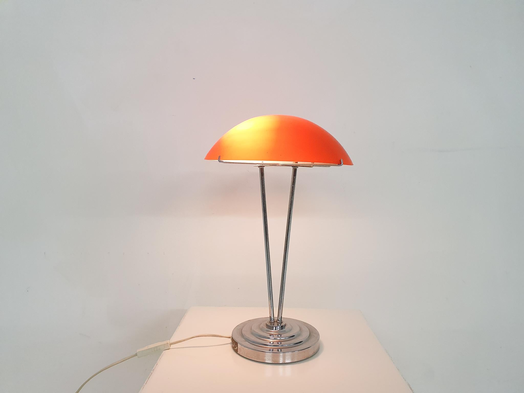 Metal desk lamp with orange glass lamp shade.