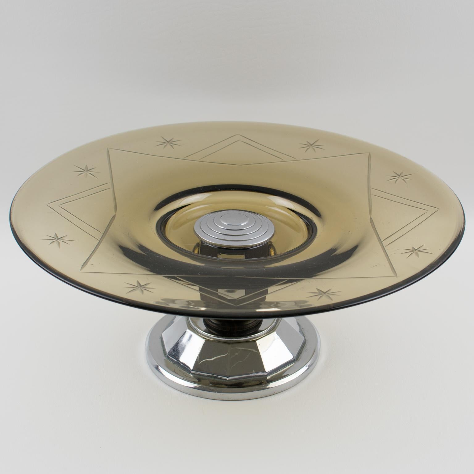 Cet élégant centre de table ou bol de service décoratif moderniste de style Art déco français présente un grand bol rond en verre avec un motif gravé dans une belle couleur gris fumée transparente. Le socle est en métal chromé et en bois de Macassar