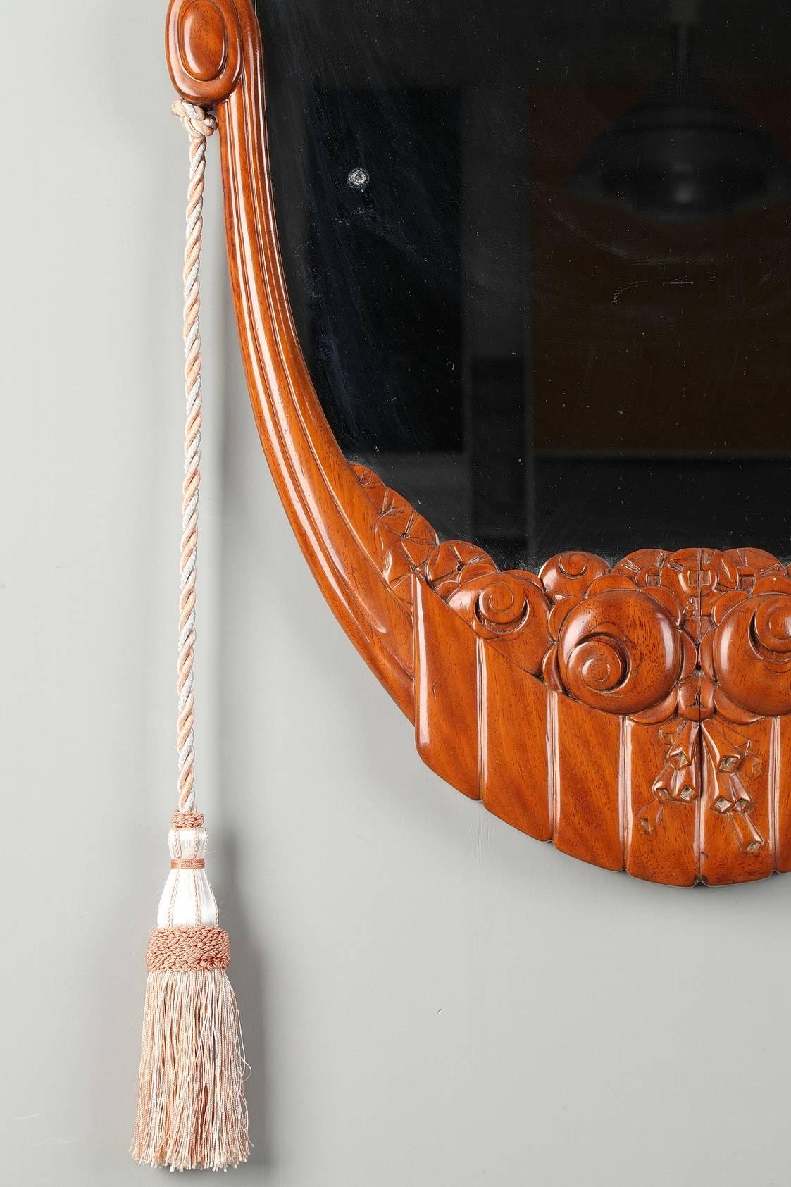 Art Deco oval glass mirror with beechwood frame decorated with floral motifs and flanked by two hanging tassels. Attributed to Maurice Dufrene. 

Maurice Dufrene (French, 1876-1955) studied at the Ecole des Arts Decoratifs in Paris, and took a job