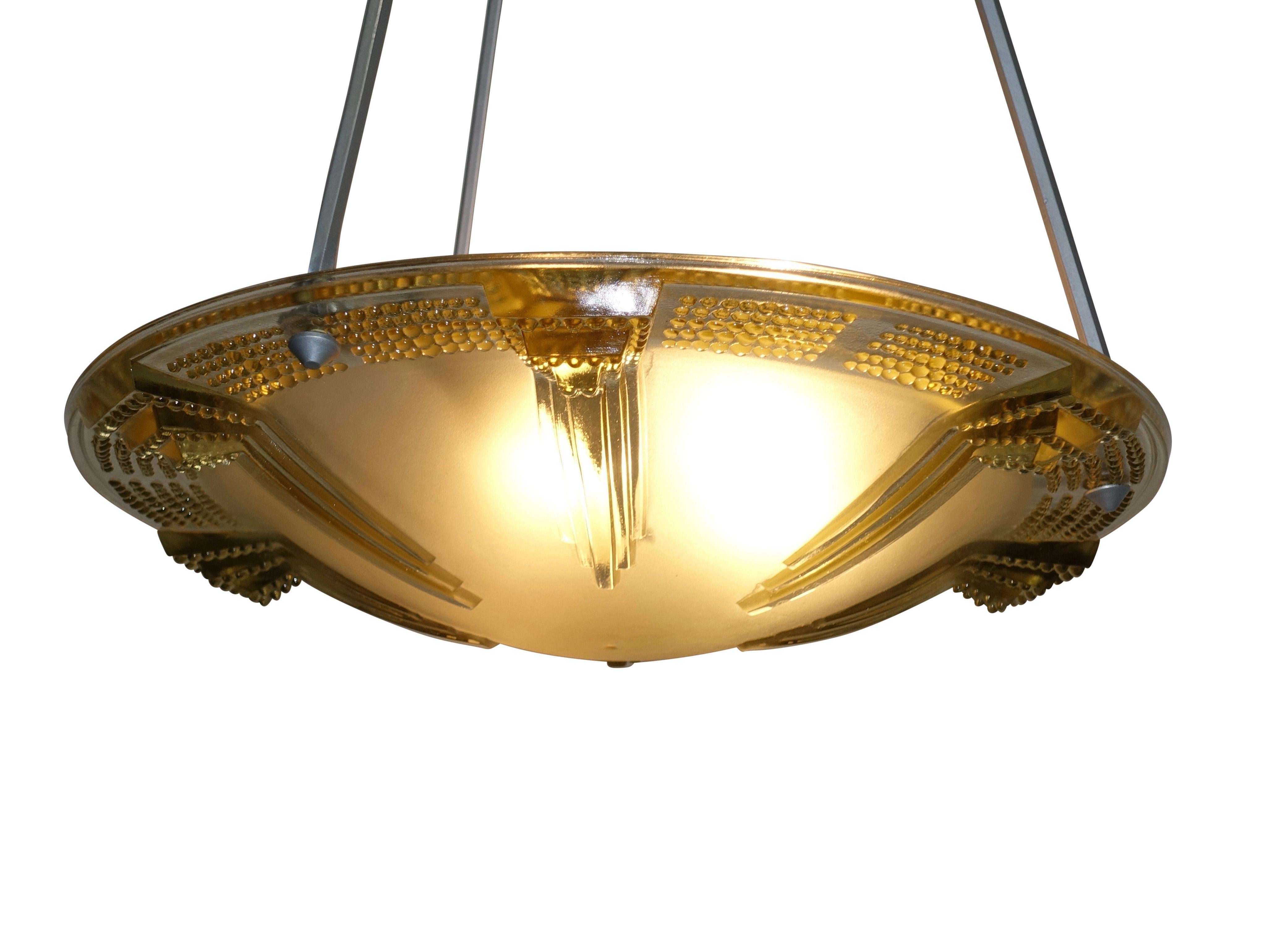 A unique greenish golden color tinted glass hanging pendant light fixture. The design is of graduated and raised towers pointing towards the center, and having a rim of graduated raised nubs, suspended from three silvered hexagonal shaped arms.