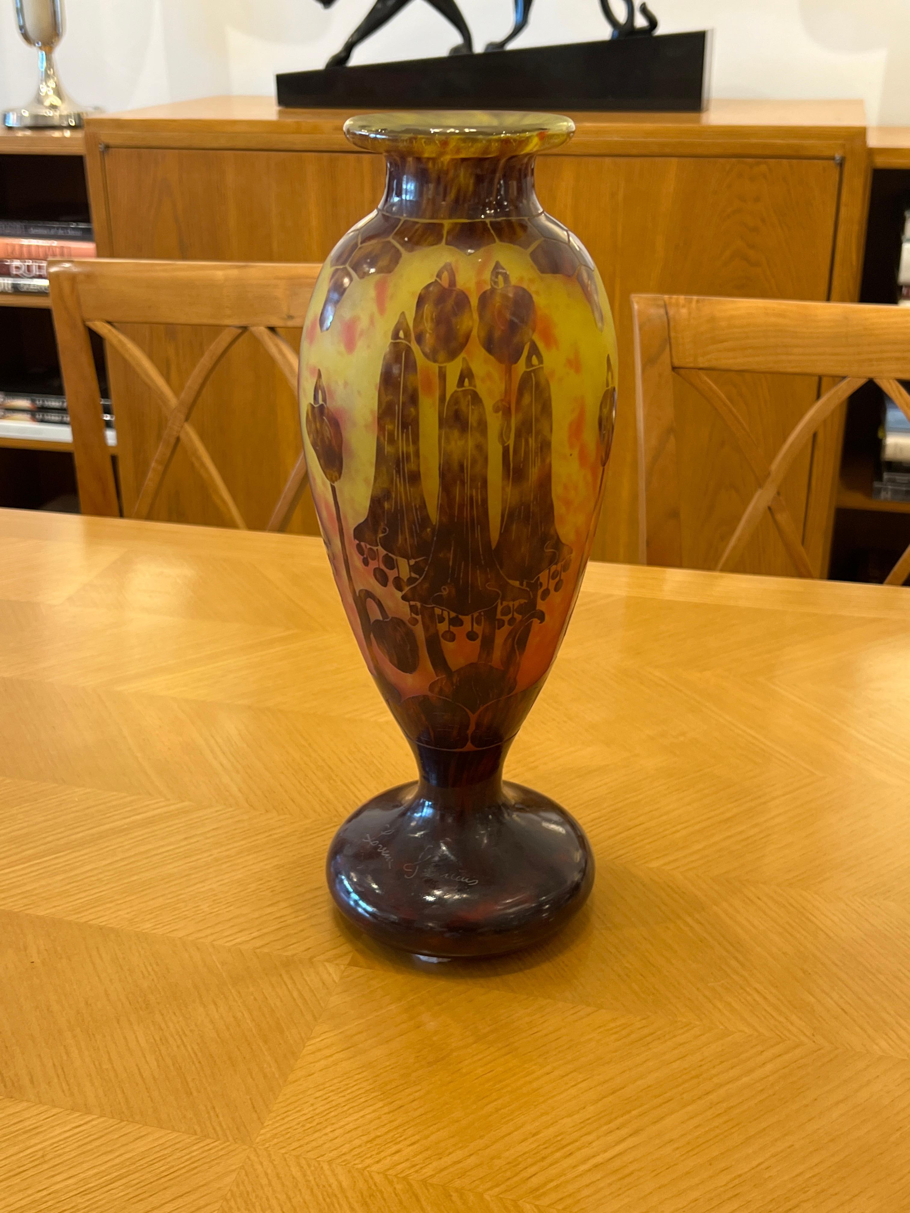 A glass vase in Mottled Yellow, Orange and Copper Red glass, overlaid with Violet.  It has a Violet and Yellow stem and foot. The pattern is acid-etched.  The floral design is from the Campanules serie by Le Verre Français.
Signature: Le Verre