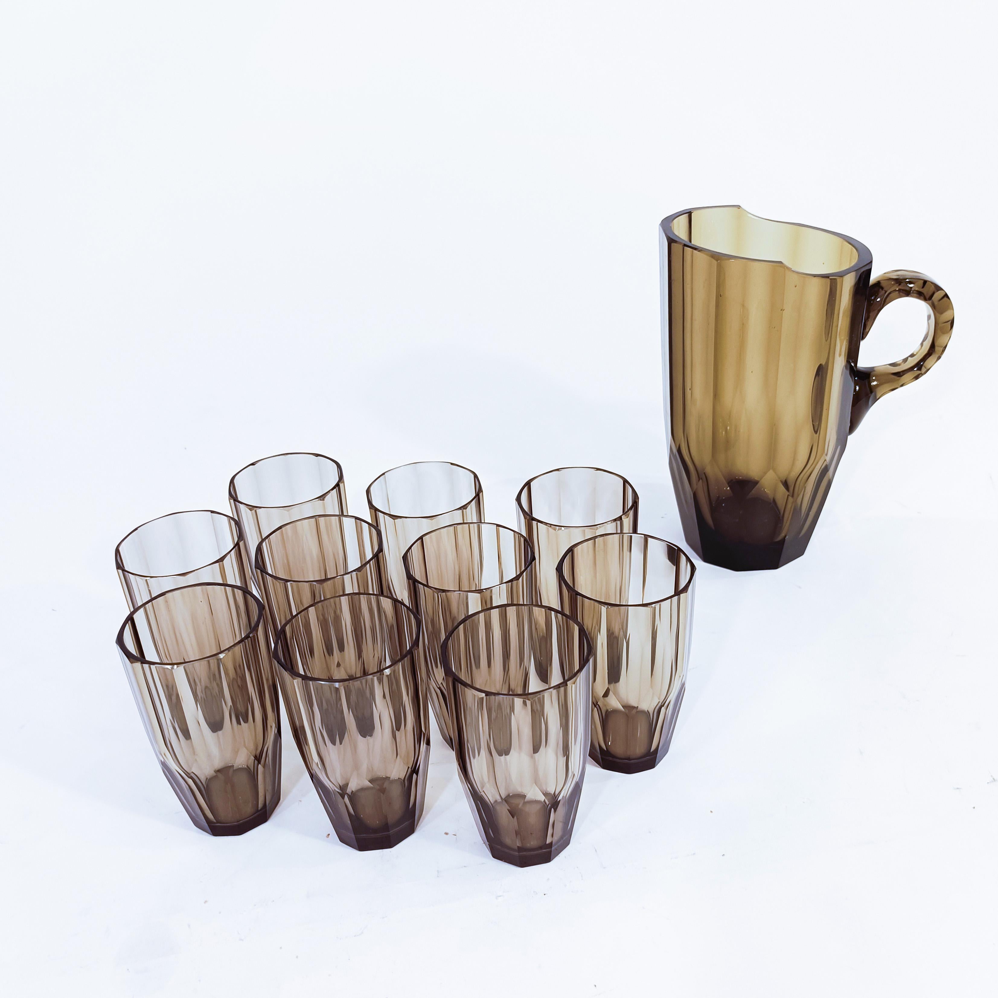 Verrerie tchèque Art déco de Moser Glassworks, années 1920. Composé de 10 verres et d'un pichet, tous en verre pressé et facetté/coupé. La couleur du verre est transparent fumé olive foncé. 
Le modèle de cette série de produits a été créé en 1928 à