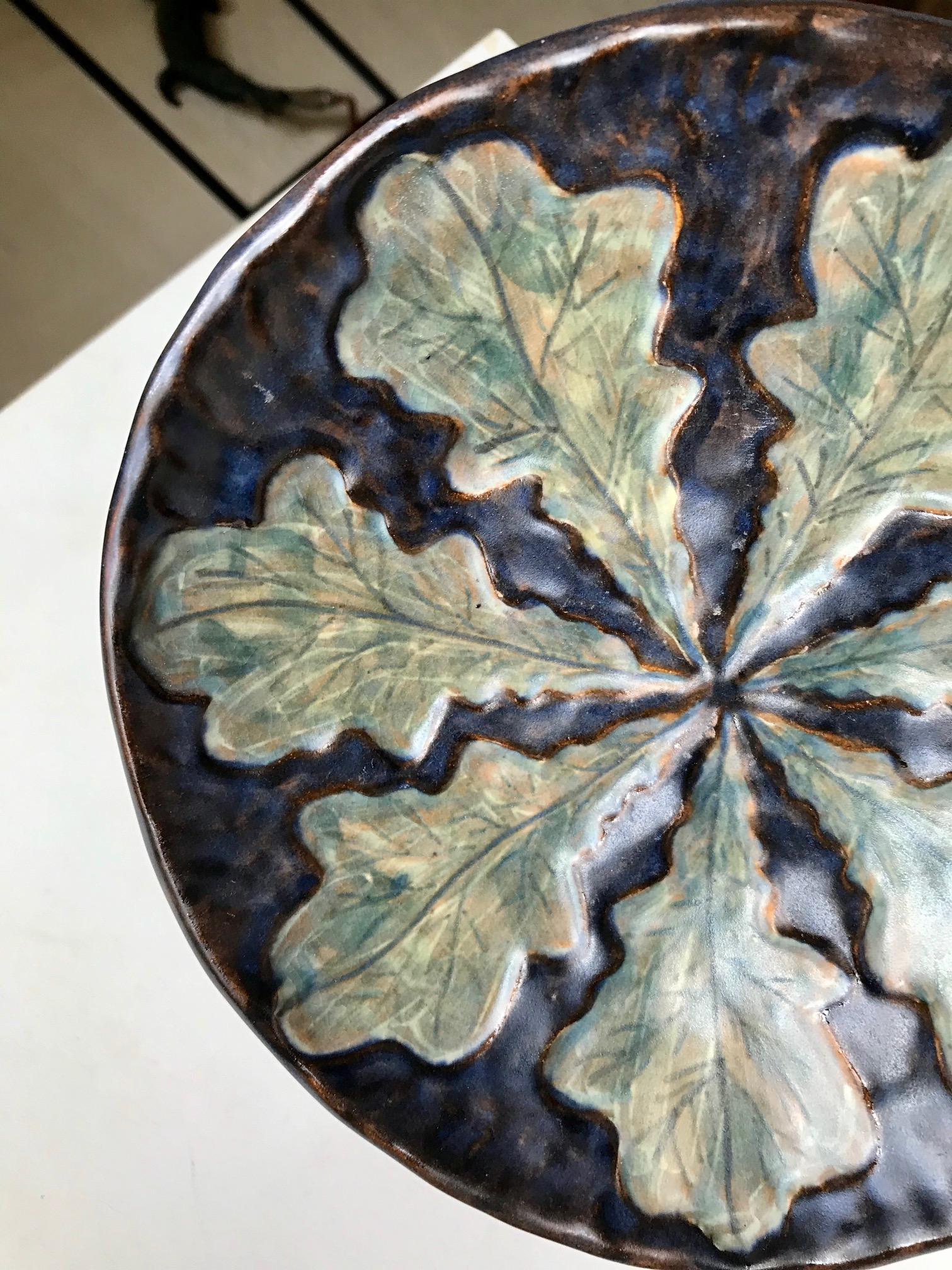 Un bol ou un plat unique avec un décor de feuilles peint à la main dans des glaçures vertes, bleues, noires et brunes. Conçu et fabriqué dans l'atelier de poterie d'Emil Ruge à Dybøl, au Danemark, dans les années 1930. Références subtiles à Thorvald