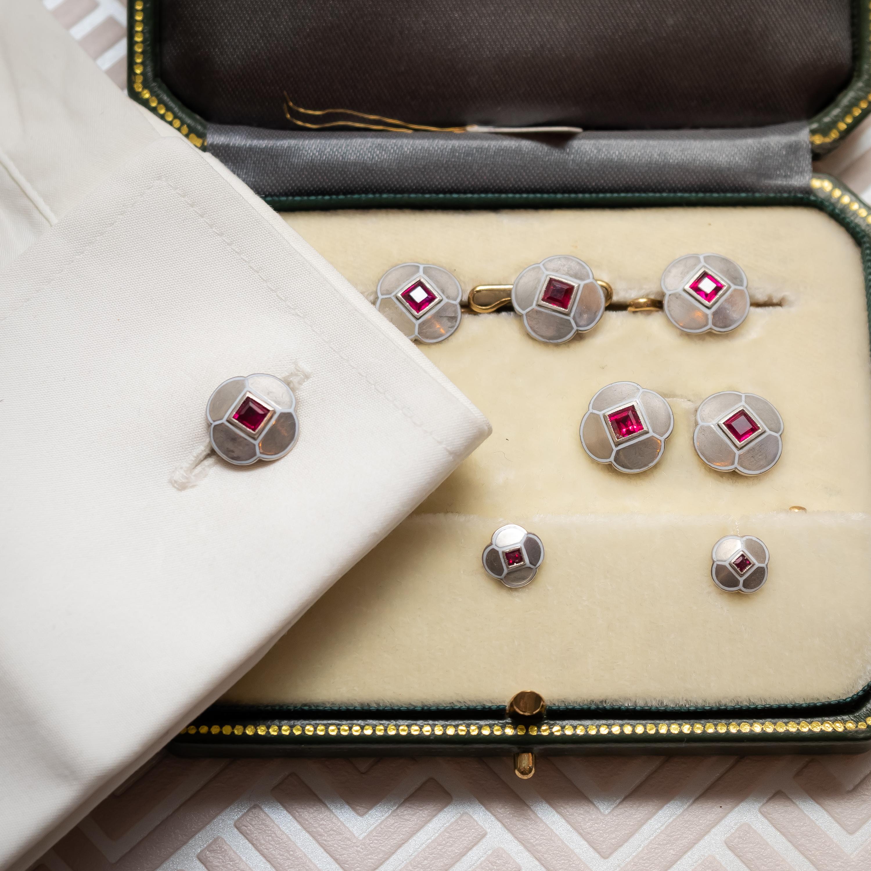 Un set da abito Art Deco in rubino, oro bianco e smalto, composto da una coppia di gemelli, quattro bottoni e tre borchie. Ciascuna maglia è incastonata con un rubino a taglio quadrato al centro e con un contorno di quatrefoglio, oro bianco e smalto