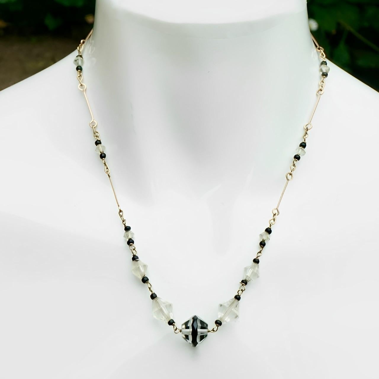 Splendida collana Art Deco in filo d'oro chiaro, con perle di cristallo sfaccettato graduate e accenti di perle nere. La perla centrale è decorata con smalto nero. Lunghezza 46,2 cm / 18,1 pollici.

Si tratta di un'insolita collana di cristallo Art