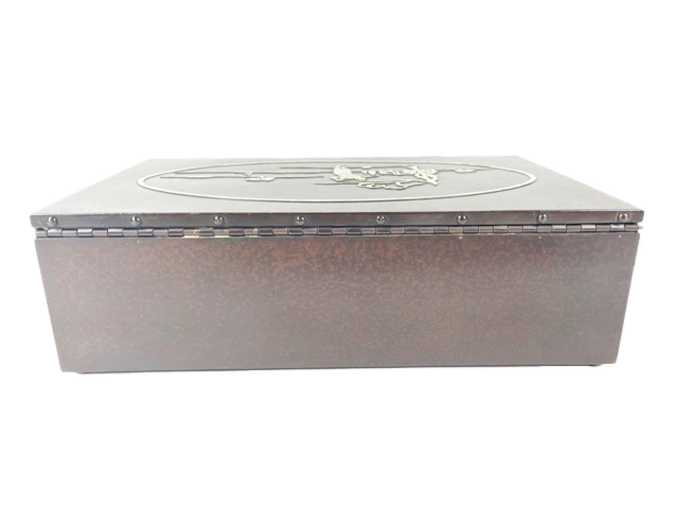 Humidor de puros Art Decó de bronce y plata de ley fabricado por la empresa Heintz Metal Art. Forrada de cedro, la caja rectangular de bronce presenta una pátina marrón moteada y la tapa tiene aplicada una escena de plata de ley con temática de
