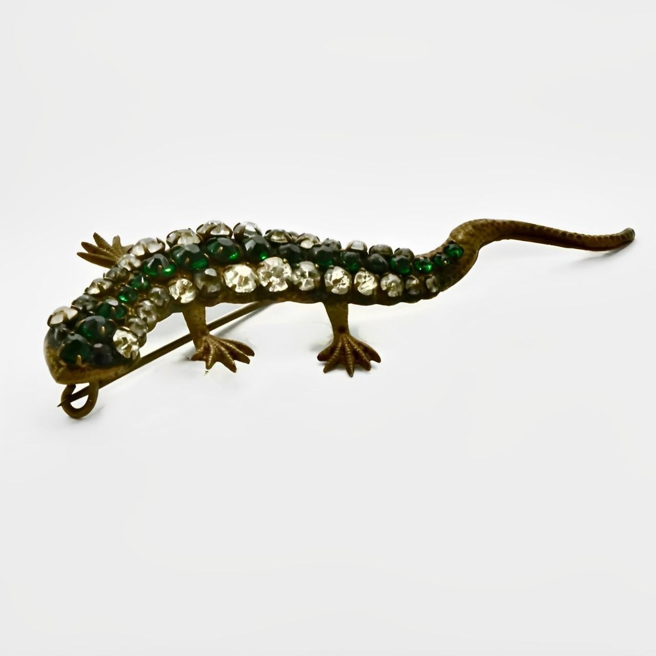 Wonderful Art Deco lizard brooch with green and clear paste stones, and red paste stone eyes. One eye has a replacement stone. The lizard was originally gold plated, it has mostly worn away to show the bronze metal underneath. Measuring length 8.2