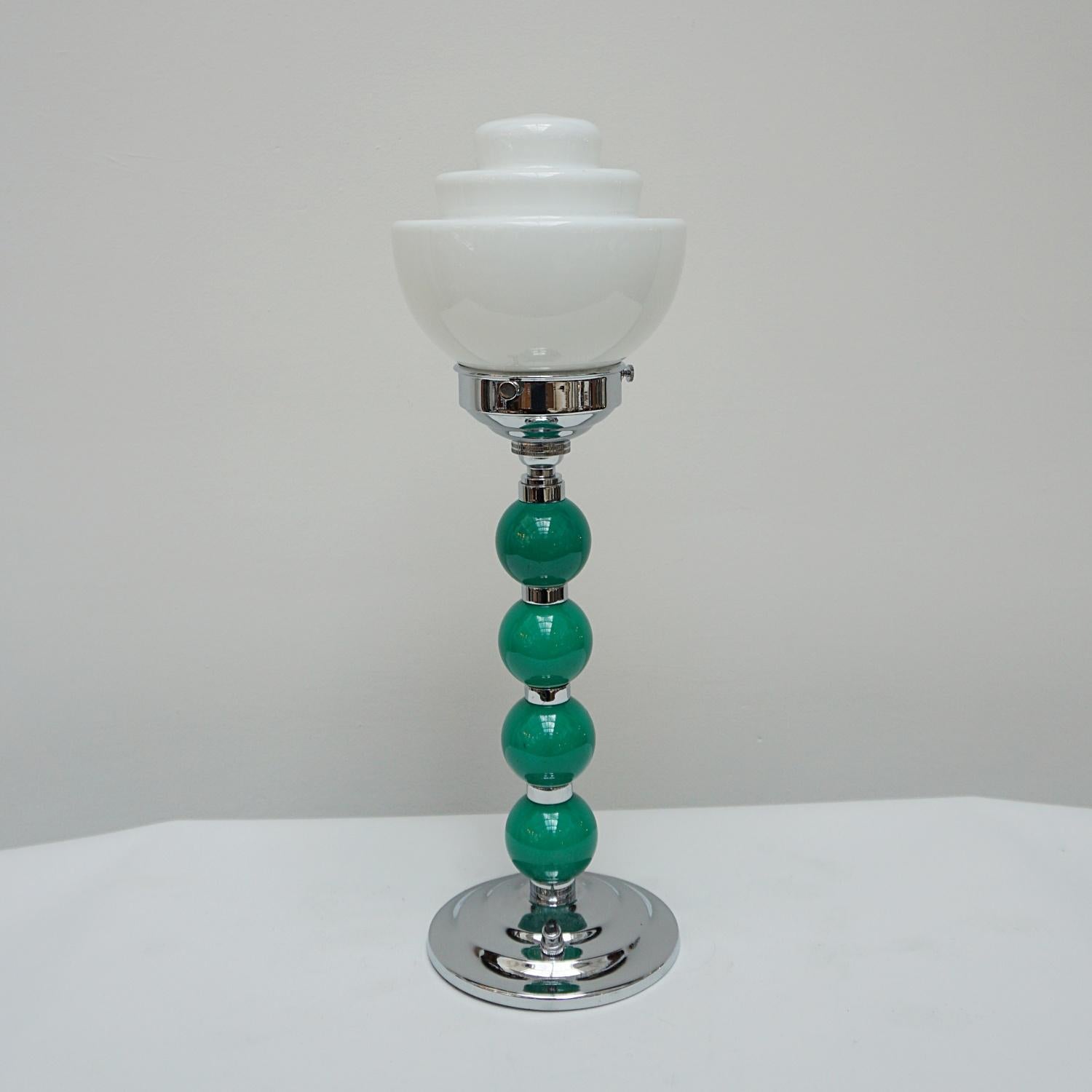 An Art Deco table lamp. Green bakelite balls with chromed banding to stem. Set over stepped circular base. White glass globe shade. 

Origin: English

All of our lighting is fully refurbished, re-wired, and re-chromed with some replacement parts.