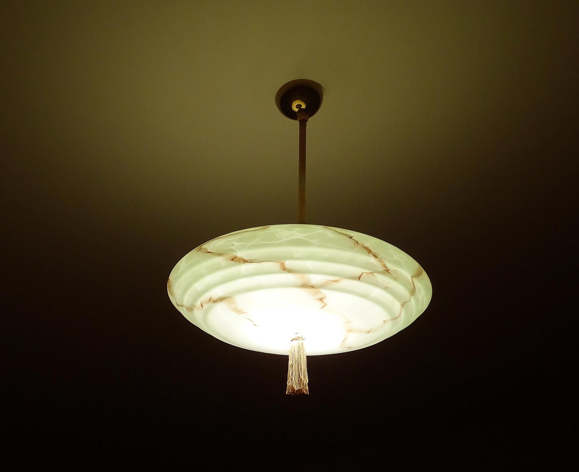 Very rare Art Deco pendant light with a stunning marbleized glass shade in UFO shape, brass stem and caps with tassel,
pole covered with thread emulating the colors of the shade
Wiring: The lamps have been tested with US American light bulbs under