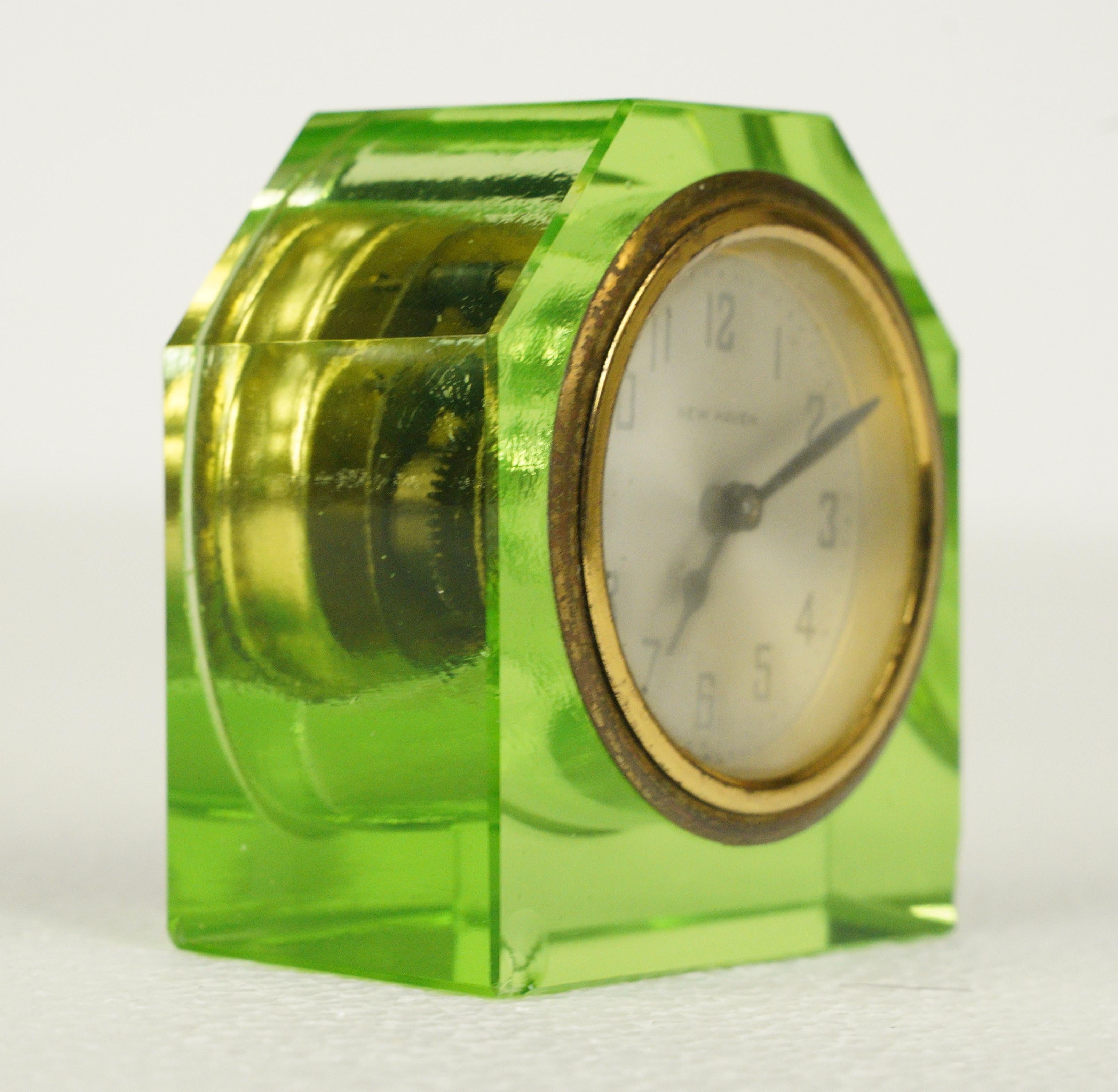 Bright green beveled uranium glass table clock with a brass rimmed face. Made by New Haven Clock Company. Good condition with very minor chips on the front and bottom left and right corners. The windup mechanism needs restoration. One available.