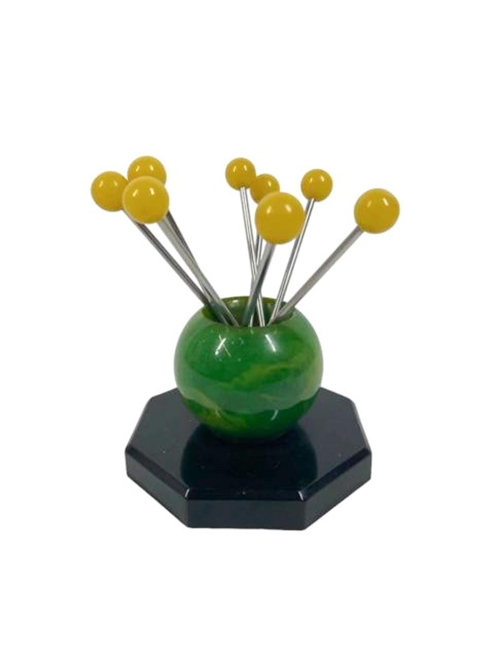 Set of 8 Art Deco chromed cocktail picks thit forked tips and yellow ball tops in a green and yellow swirled Bakelite ball shaped stand on an octagonal black Bakelite base.