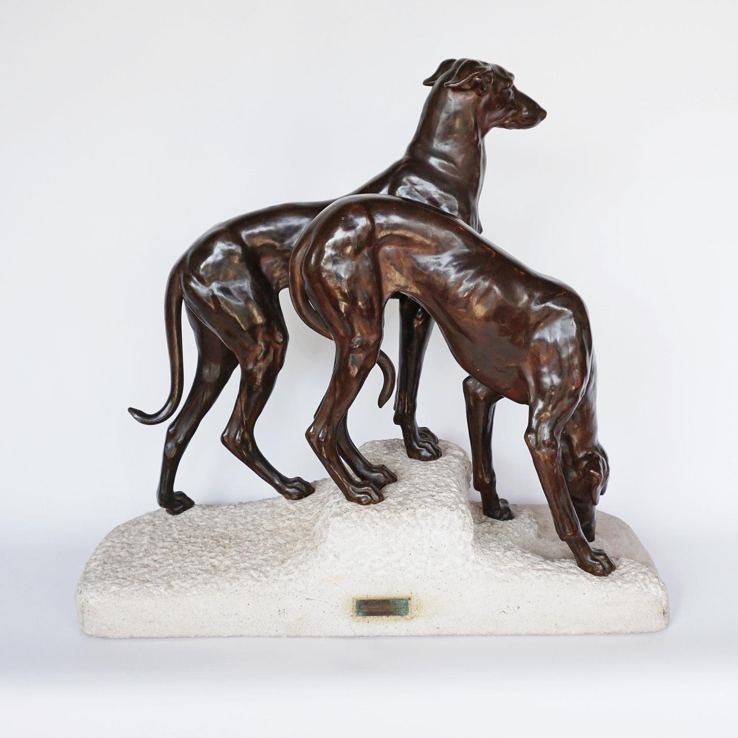 An Art Deco sculpture group by Jules-Edmund Masson (1871-1932) depicting two Greyhounds on a rocky base, the female drinking from a small pool whilst the male dog stands erect. White art metal with a bronze patinated finish. Set over a limestone
