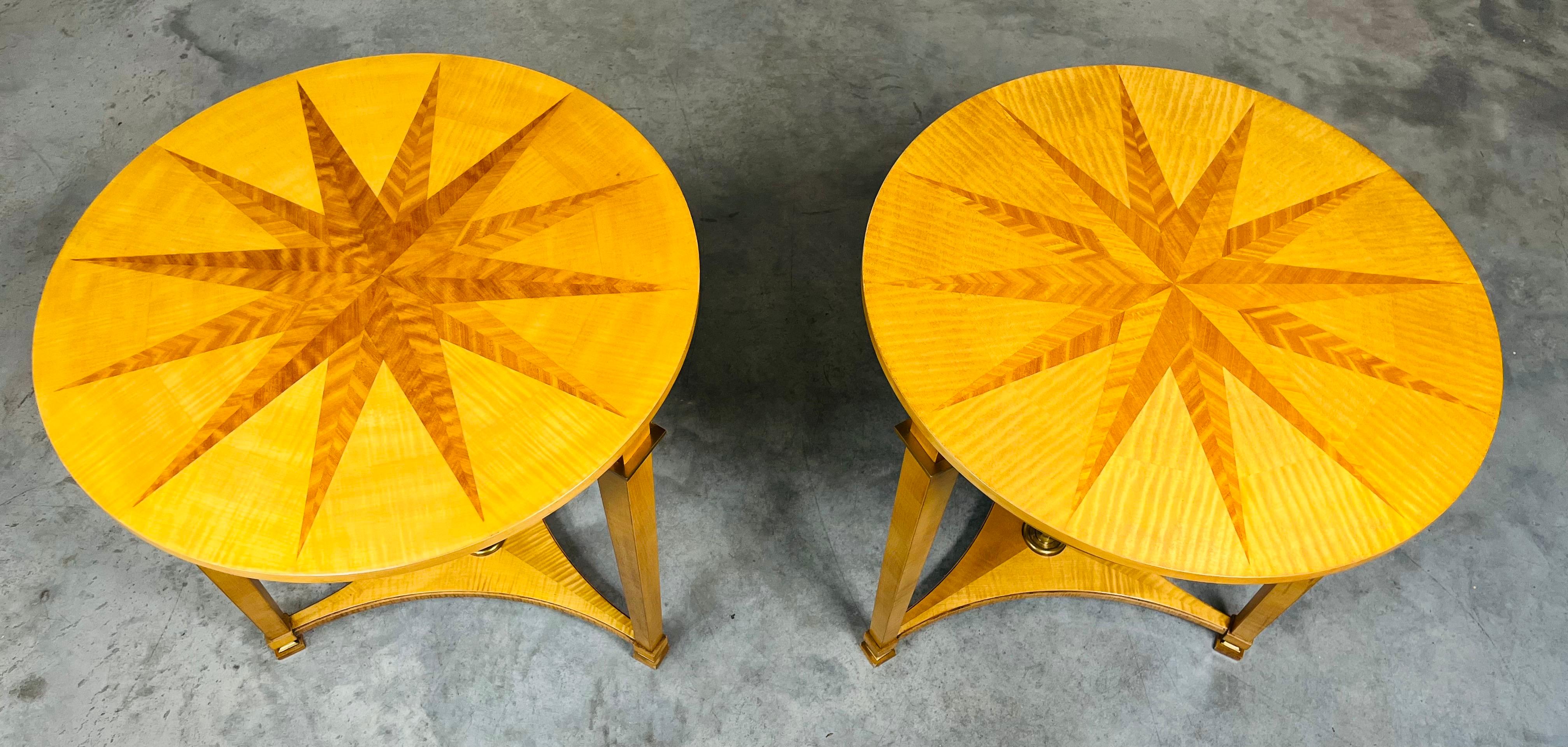 A stunning pair of Neoclassical Guéridon tables from Baker’s Andre Arbus Collection having starburst parquetry sycamore and maple tops with tapering column legs with brass accents over sculptural bases that feature a regal brass ring that ties the