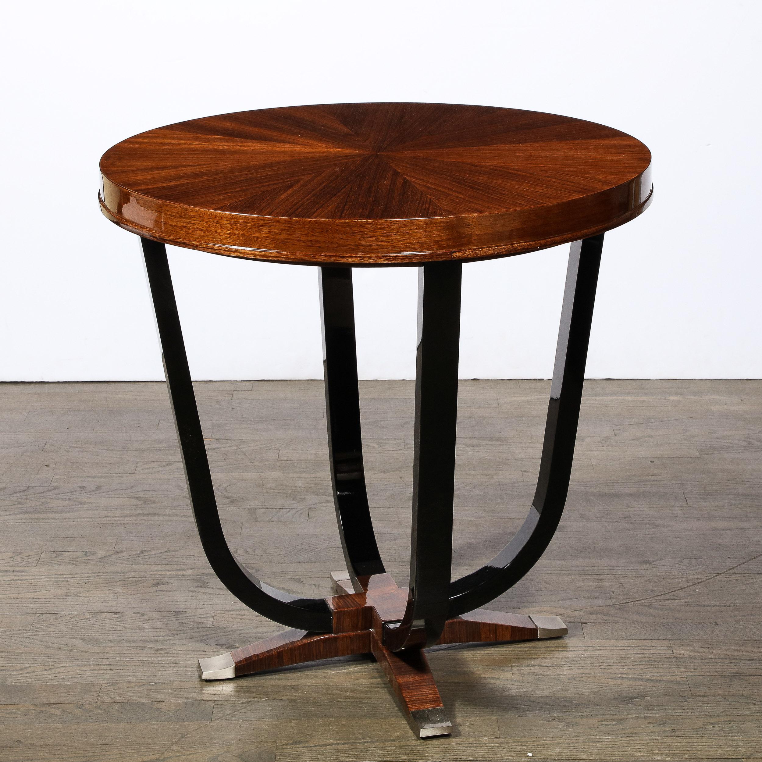 This stunning Art Deco Gueridon table was realized in France circa 1935. It features a four-pointed base in bookmatched walnut capped on the ends with brushed nickel sabots. Four streamlined supports ascend upwards in black lacquer where they