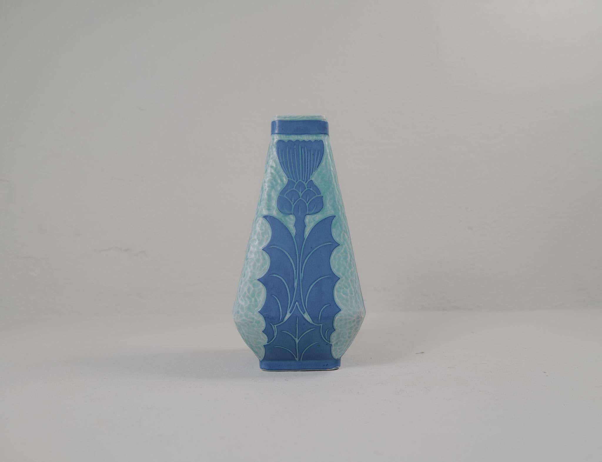 Sgraffito-Vase im Art déco-Stil mit Blumenmotiv, von Josef Ekberg für Gustavsberg.
Sgraffito ist eine Art, zwei Schichten zu einem Muster zu verbinden. Die zweite Schicht wird abgekratzt und übrig bleibt ein hellblauer Hintergrund mit einem schönen