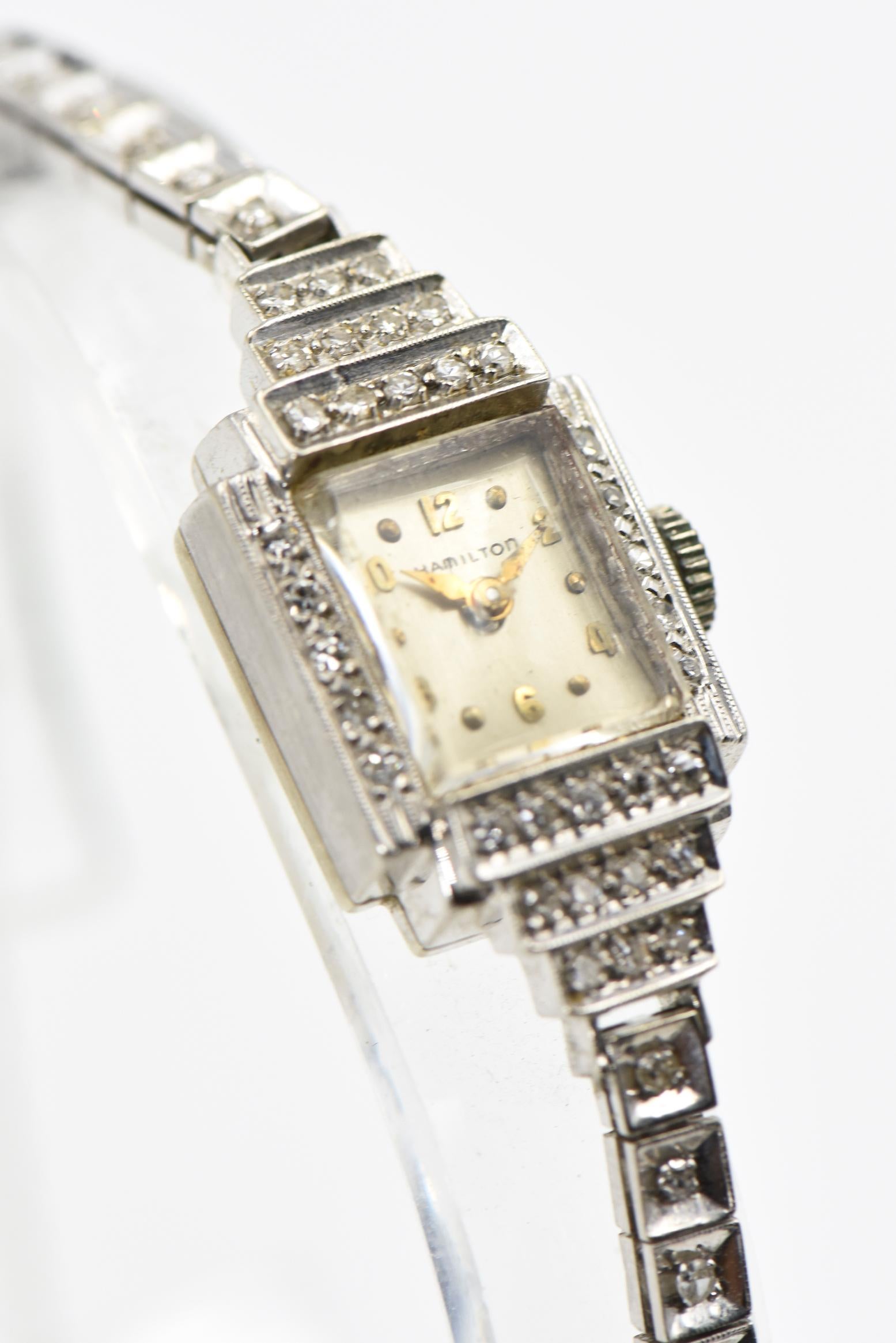 Elegant Hamilton ladies evening wrist watch featuring a rectangular face within a diamond frame.  The top and bottom have a graduated deco step design.  The band has square links with prong set diamonds inside each link.  The band terminates with a