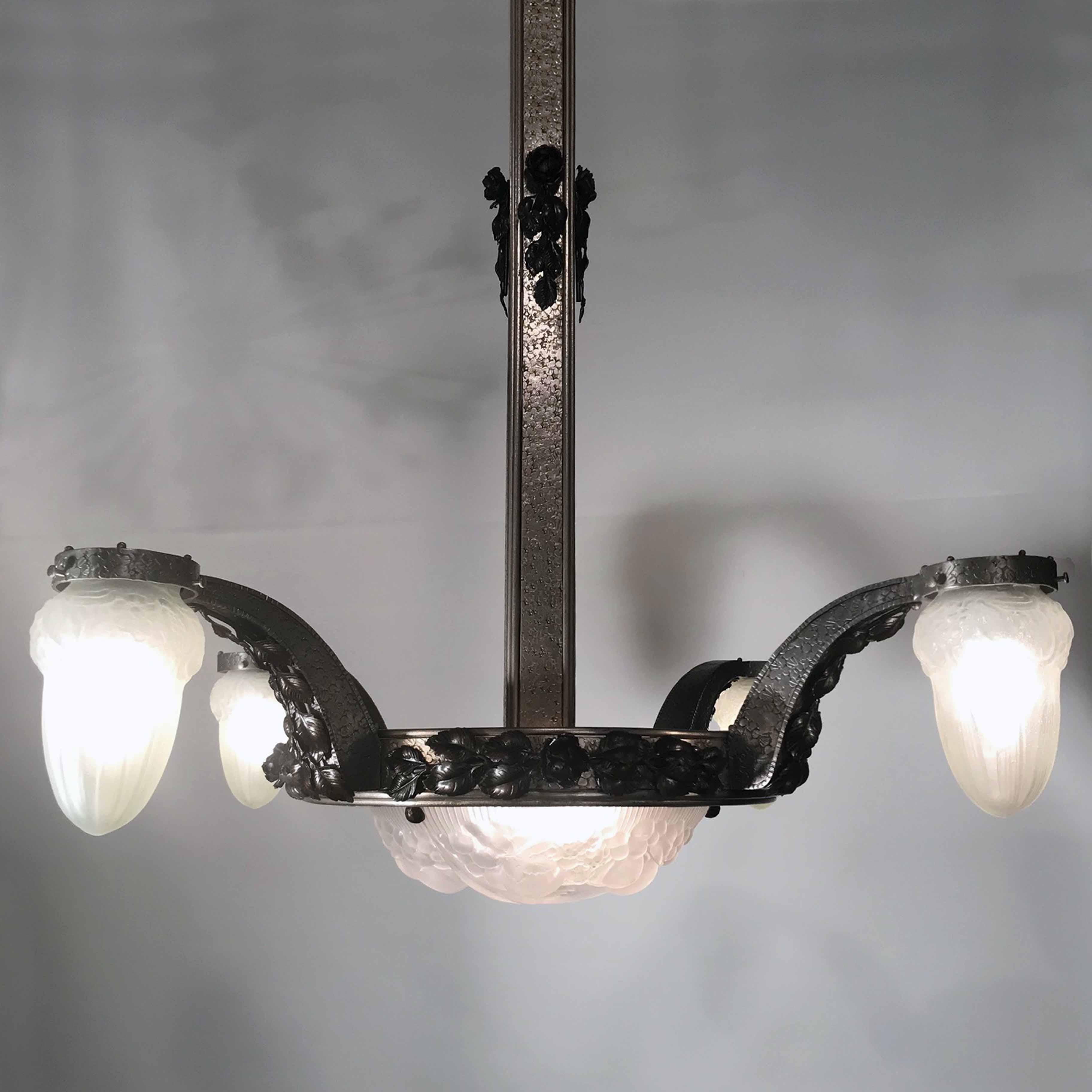 This Period Art Deco chandelier is steel with a multi textured martele finish to the stem and four shaped arms applied with leaves and floral ornament. The frosted shades and bowl are molded with berries and leaves. The contrast between the hardness