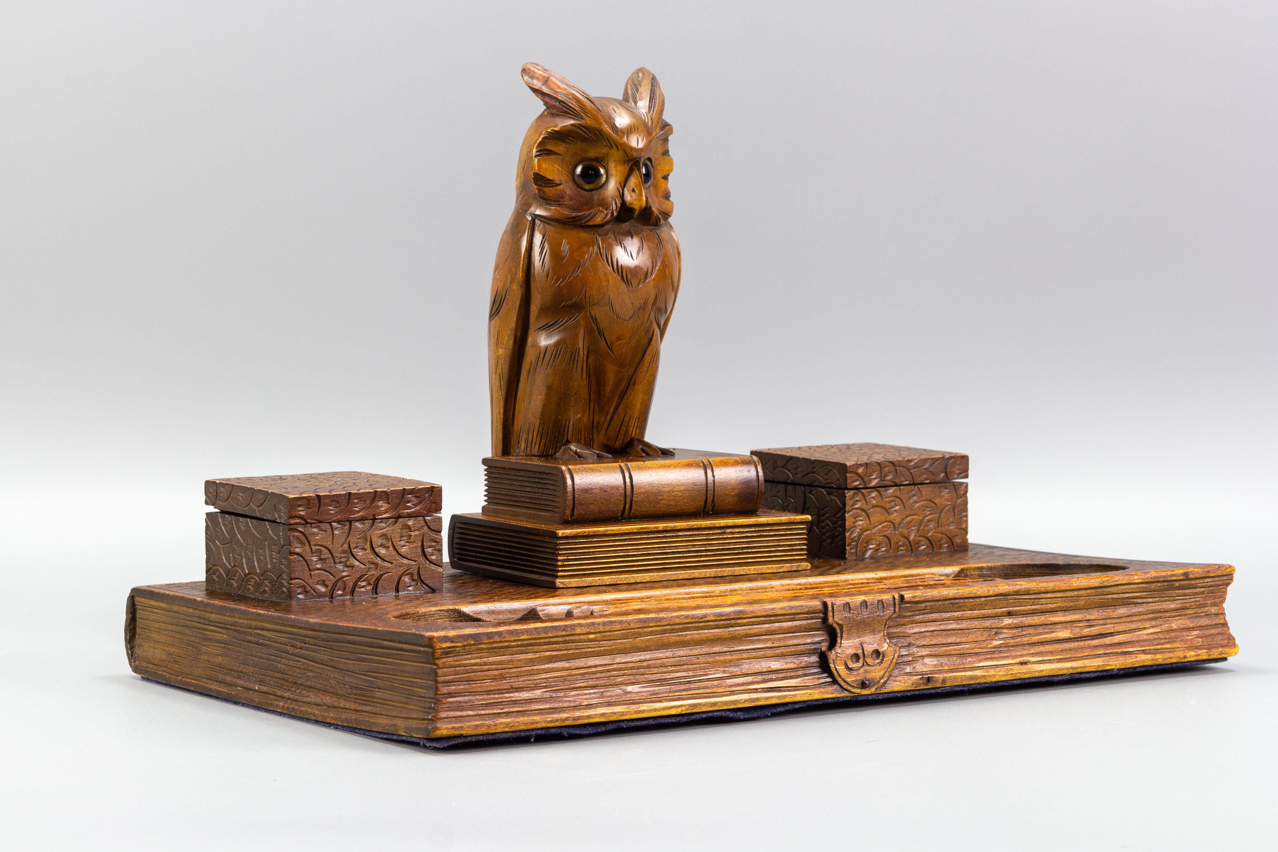 Beautiful Art Deco hand-carved wooden double inkwell in a shape of a book with a majestic owl figure sitting on two books. The inkwells contain the original white porcelain liners. The owl has glass eyes, and the Stand has trays for pens and
