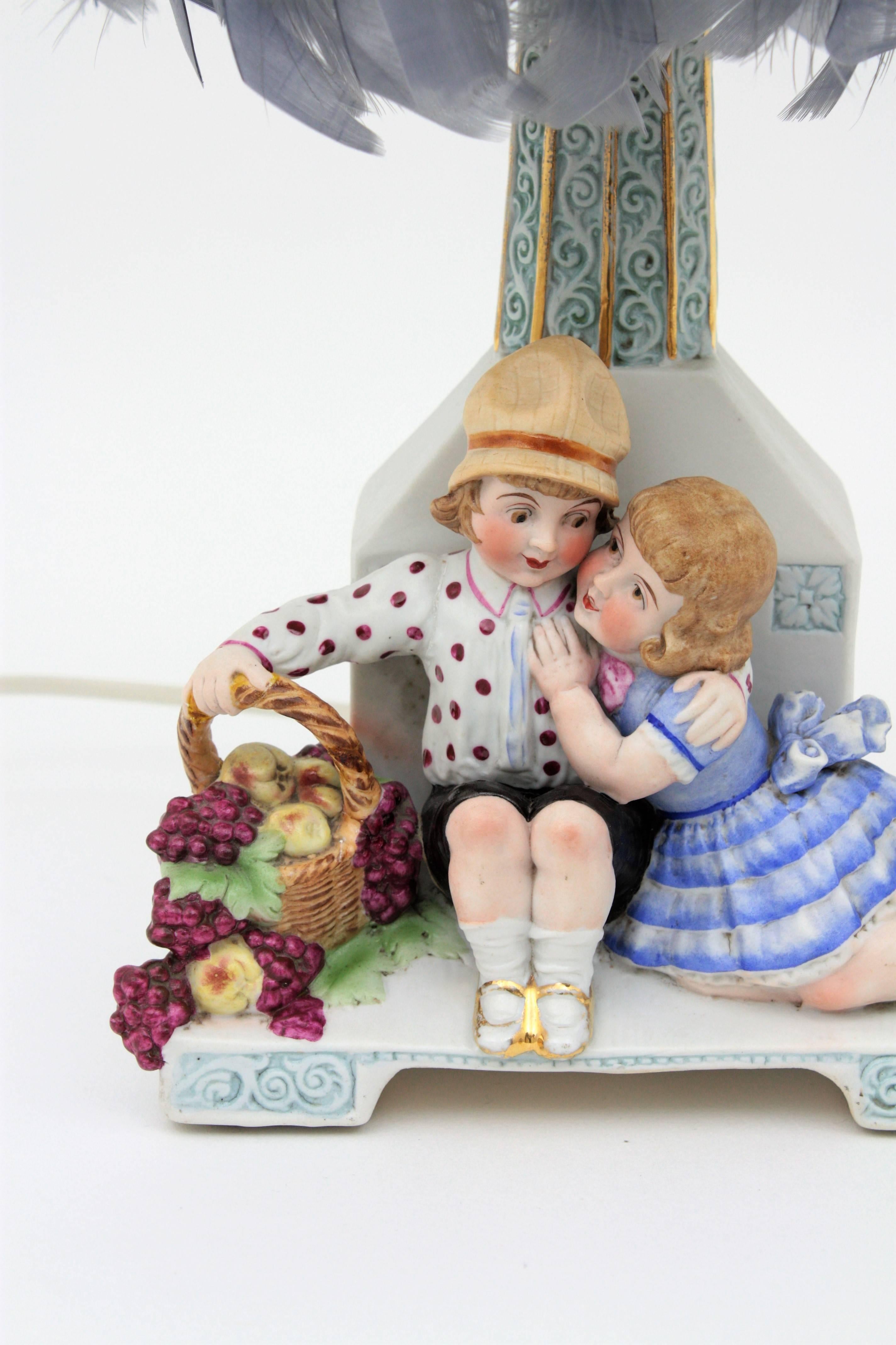 A lovely hand painted biscuit porcelain table lamp with children figures wearing a fruit basket with feathers silk shade. England, 1930s.
The column holding the lamp has a beautiful decoration with engraved pattern painted in baby blue color with