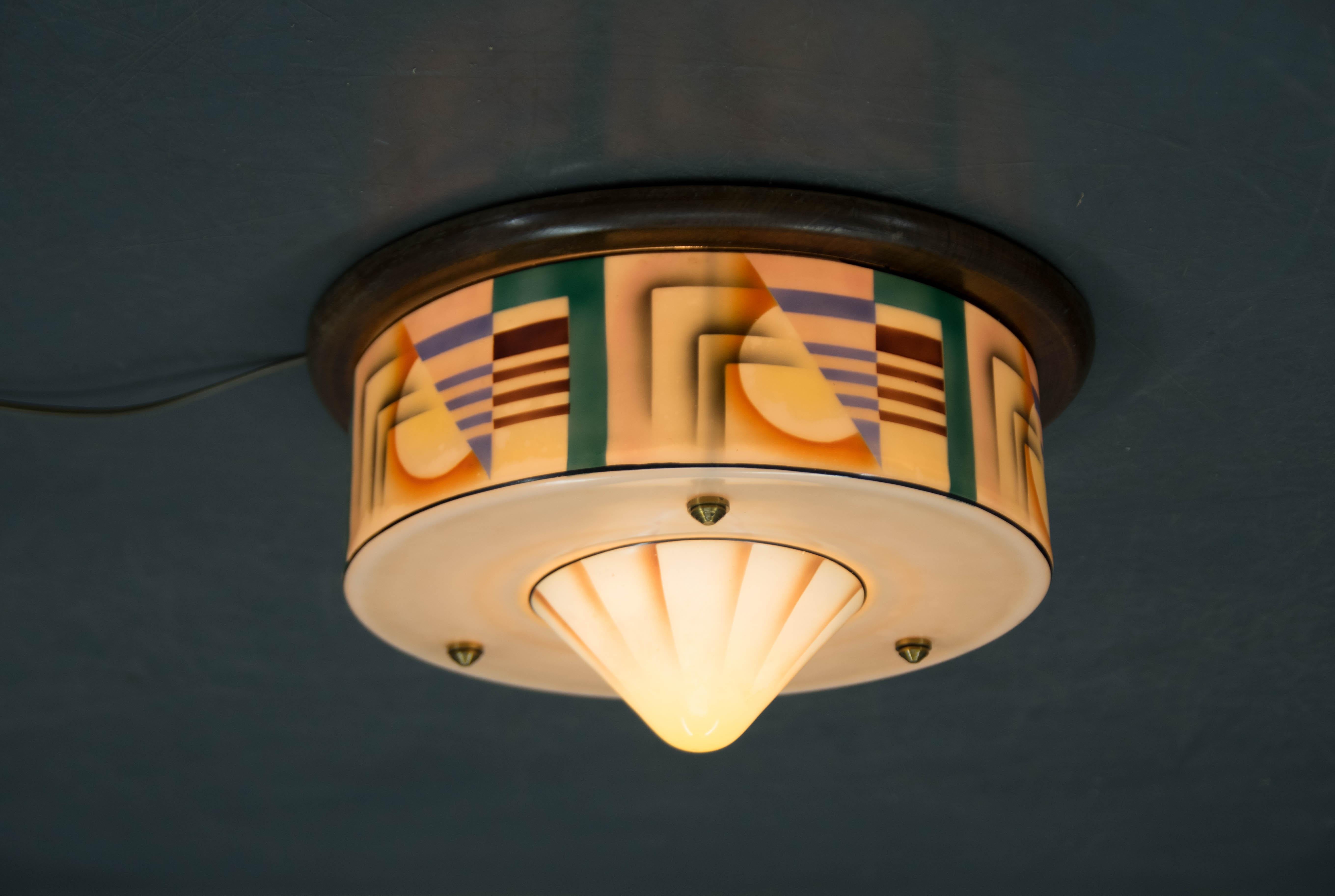 Aggiungi un tocco di eleganza senza tempo al tuo spazio con questa esclusiva plafoniera da incasso Art Deco. L'apparecchio presenta un paralume in vetro dipinto a mano con un sorprendente motivo geometrico e colori dai toni caldi che evocano la