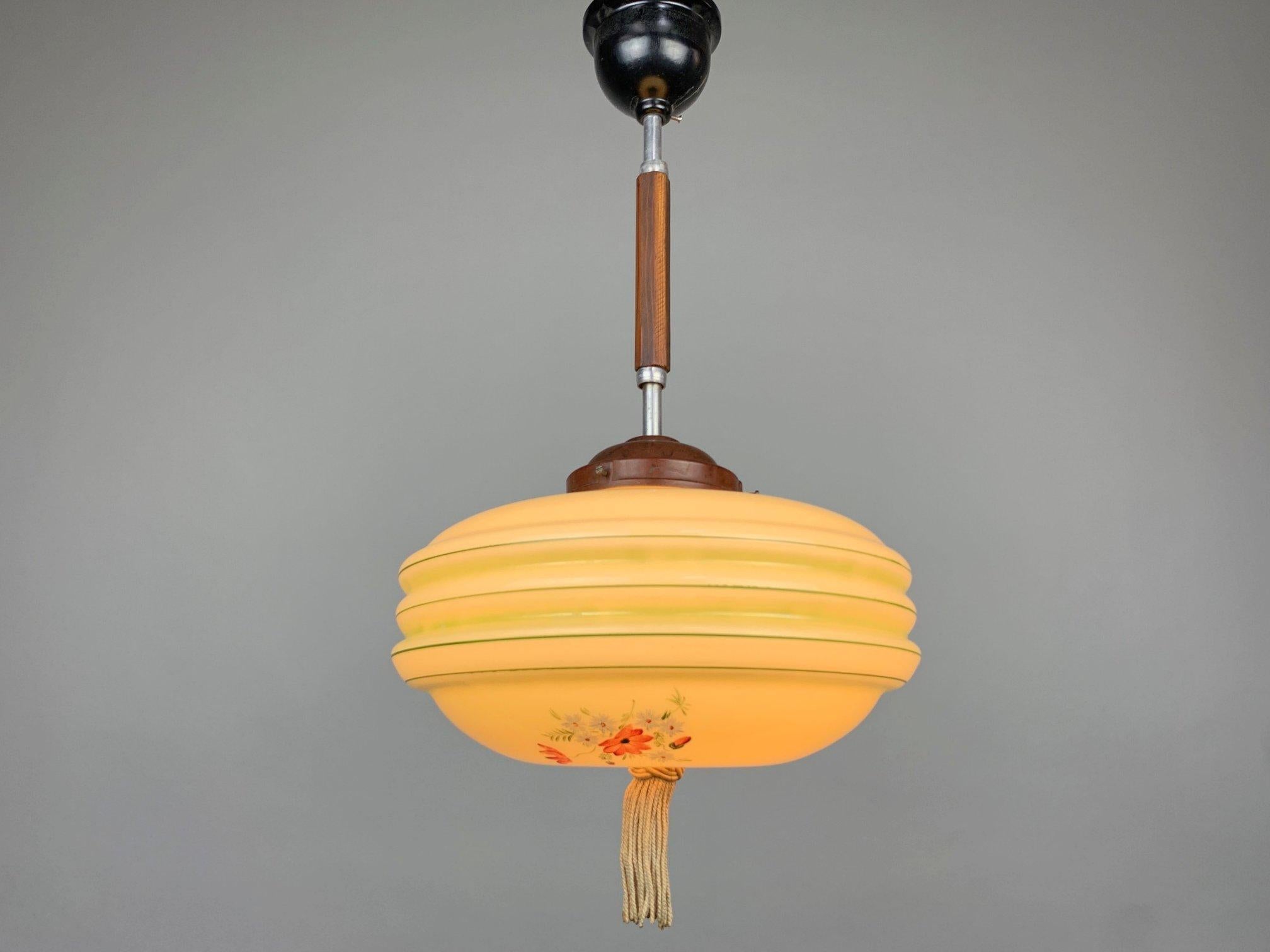 A beautiful Art Deco pendant with a handmade glass shade decorated with hand painted floral motifs, an original hand tied tassel and wooden decoration on the bar. There is a crack on the chandelier top (see photo). 
Bulbs: 1 x E27 or E26.