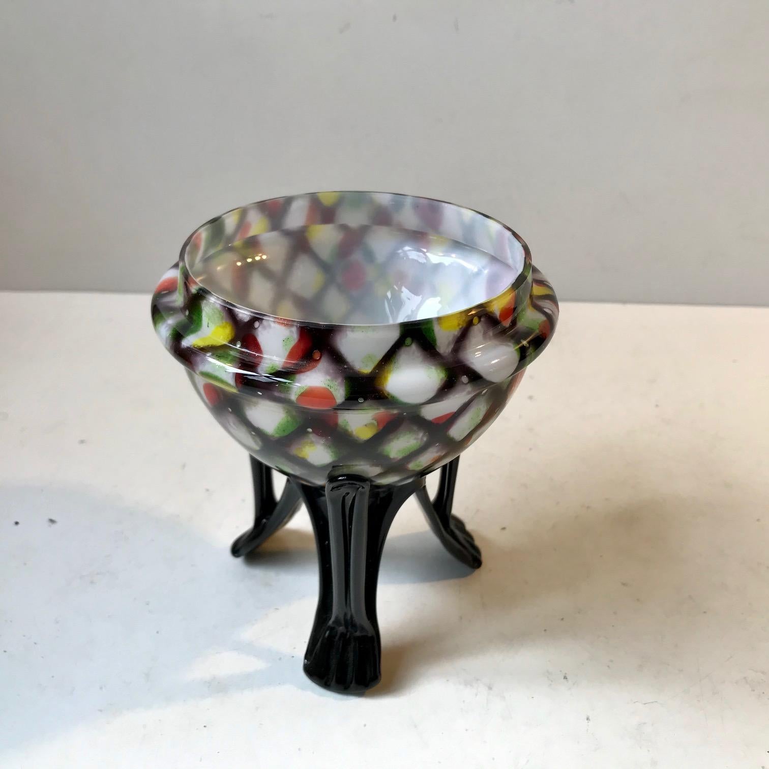 A handblown posy vase with a top part in harlequin pattern spatter glass cased upon white opaline glass. Its base is made from black glass shaped by hand. It was made during the 1930s in Bohemia/Czech Republic by Franz Weltz.