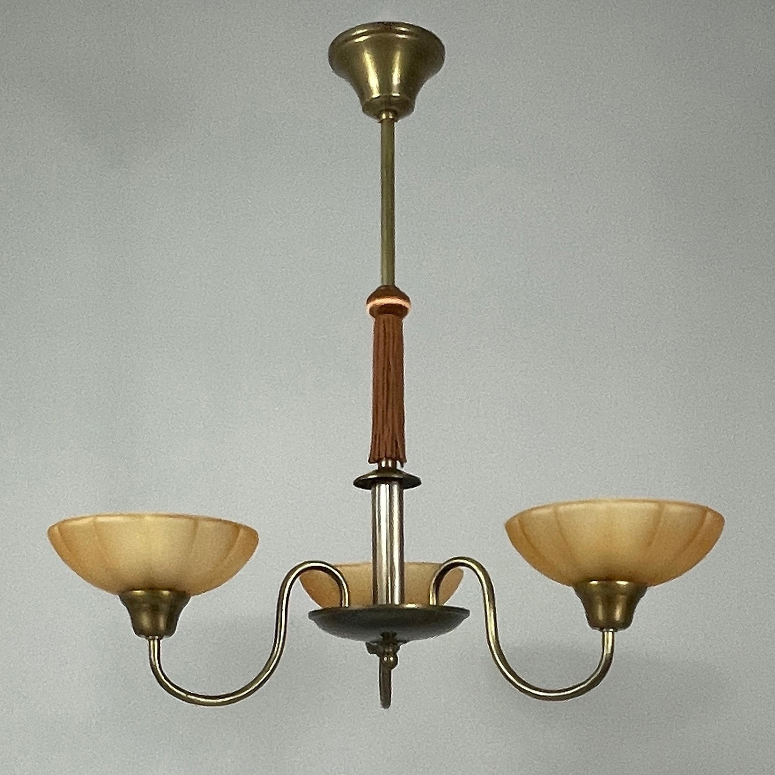 Swedish Grace Chandelier, 1930s

The light features a distinctive 1930s Swedish design with an elegant brass frame and gracefully curved arms supporting three frosted Havanna glass shades. 

A central rod extends from the ceiling mount, adorned with