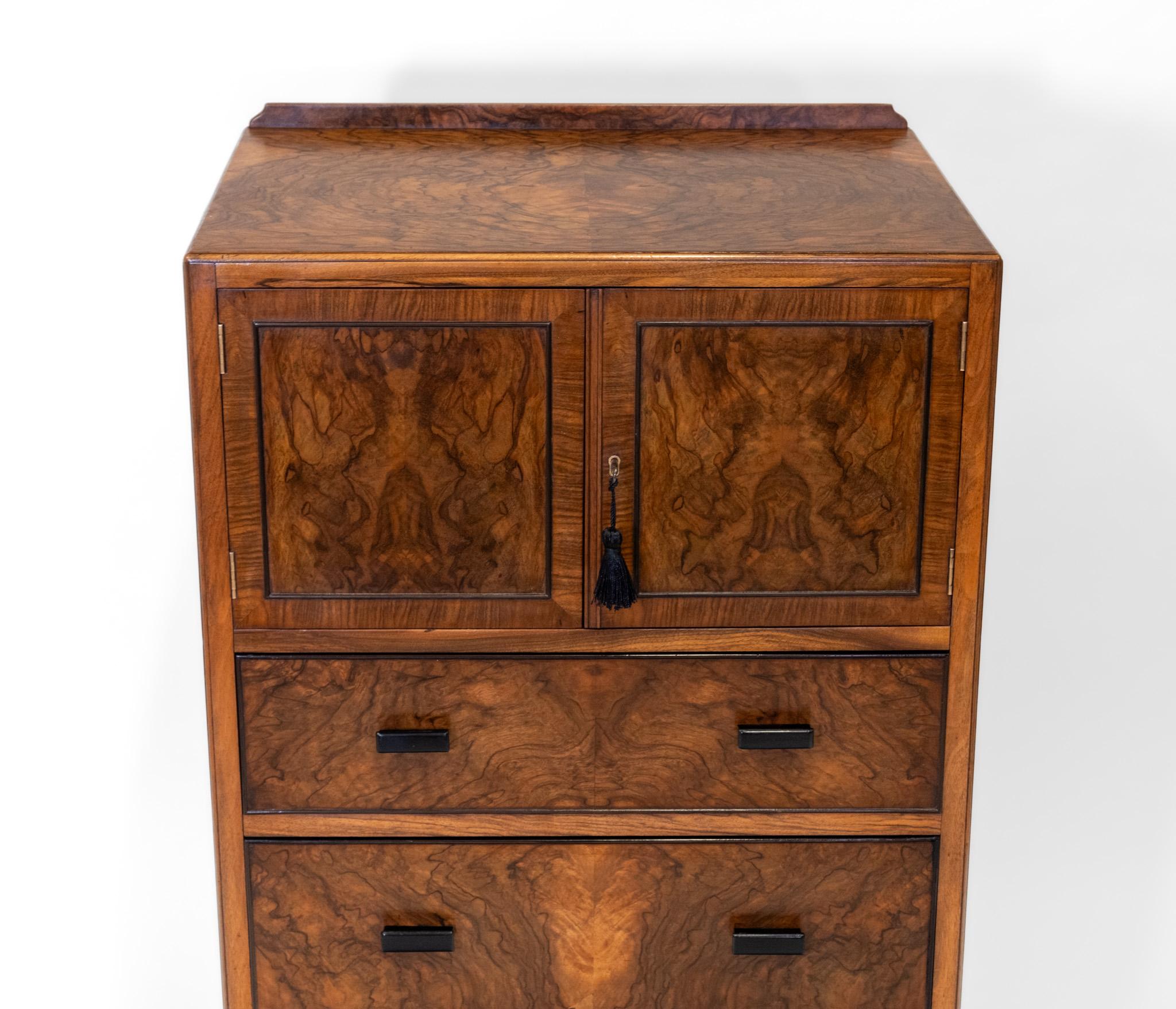 A wonderful Art Deco figured walnut and contrasting ebonised detail tallboy of small proportions. Retailed by Heal's of London. Labelled. Circa 1930.

Of excellent quality, with highly figured book match walnut, veneered over solid mahogany. Solid