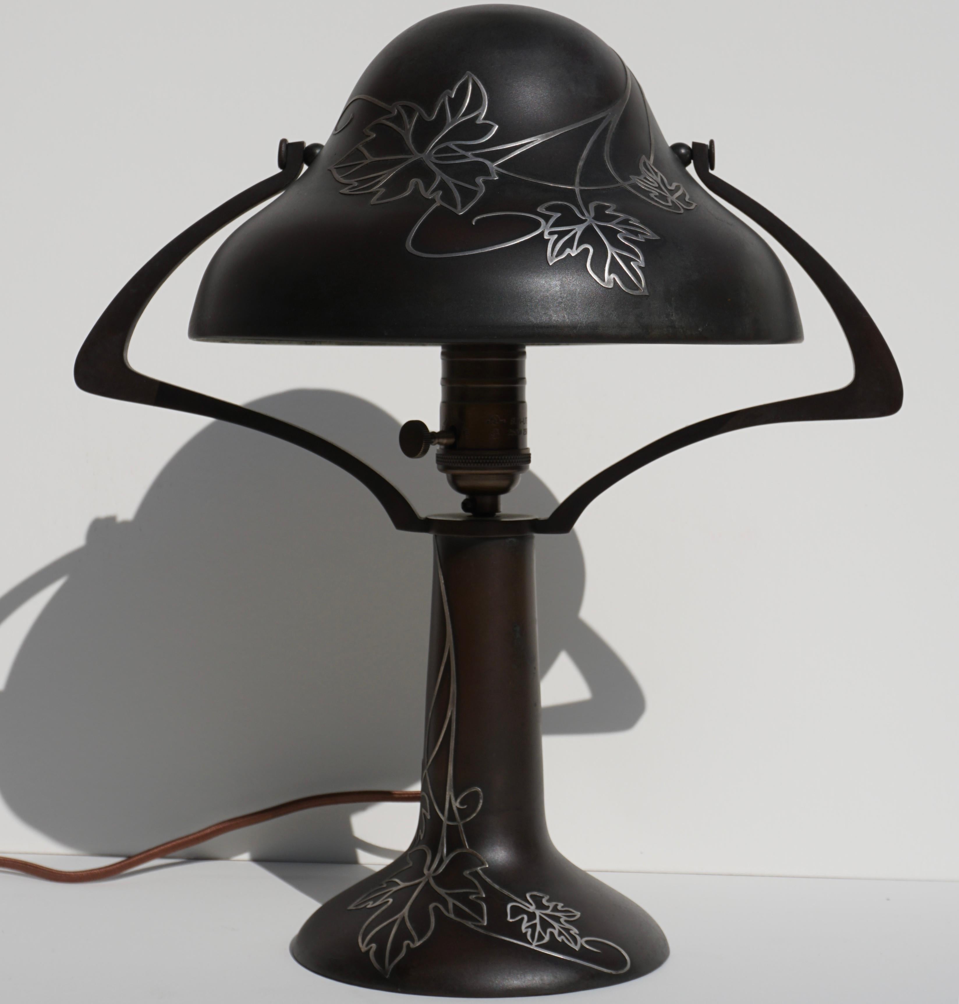 A Heintz patinated bronze and silver overlay table lamp, circa 1920 Art Nouveau, Art Deco, Arts & Crafts design. Shade and base are made of bronze with silver overlay perfect as a desk or bedside table lamp emitting a beautiful soft glow. Wired and