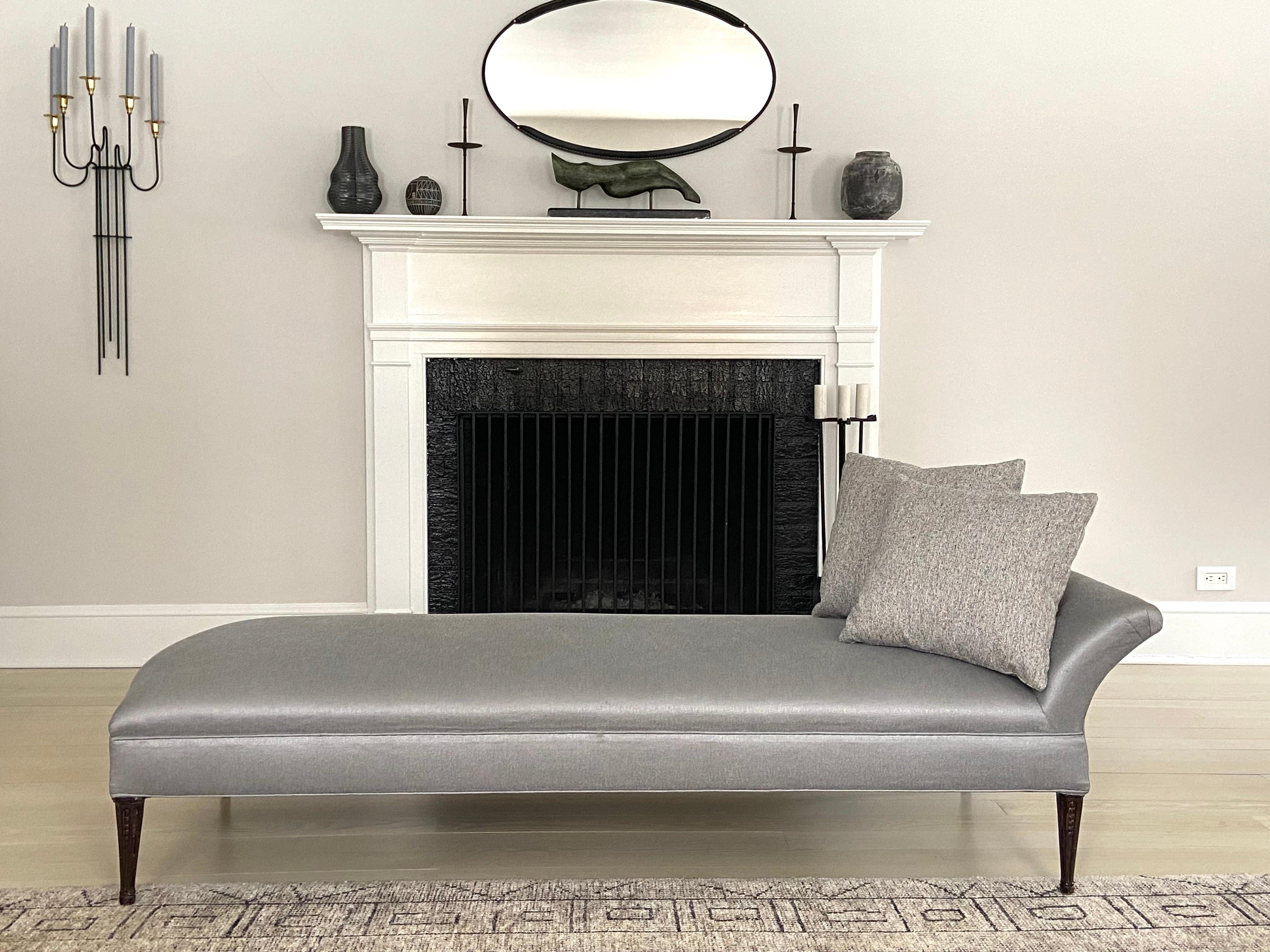 An elegant and glam 1940s Hollywood Regency sculptural chaise with tapered carved legs. Newly upholstered in a shimmery silver fabric. The wood legs are carved. The pillows in one of the photos are not included but are showing how you can dress it