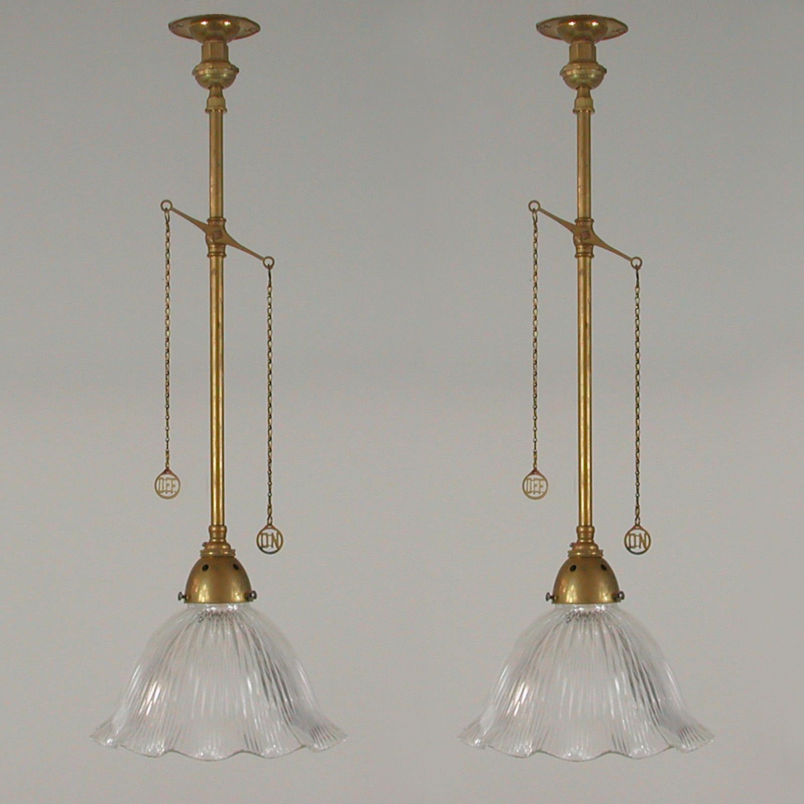 These unusual vintage pendants were designed and manufactured in England in the 1920s. They feature clear glass Holophane style tulip shaped lamp shades and naturally aged brass details. The lights appear to have been converted from old gas lamps in
