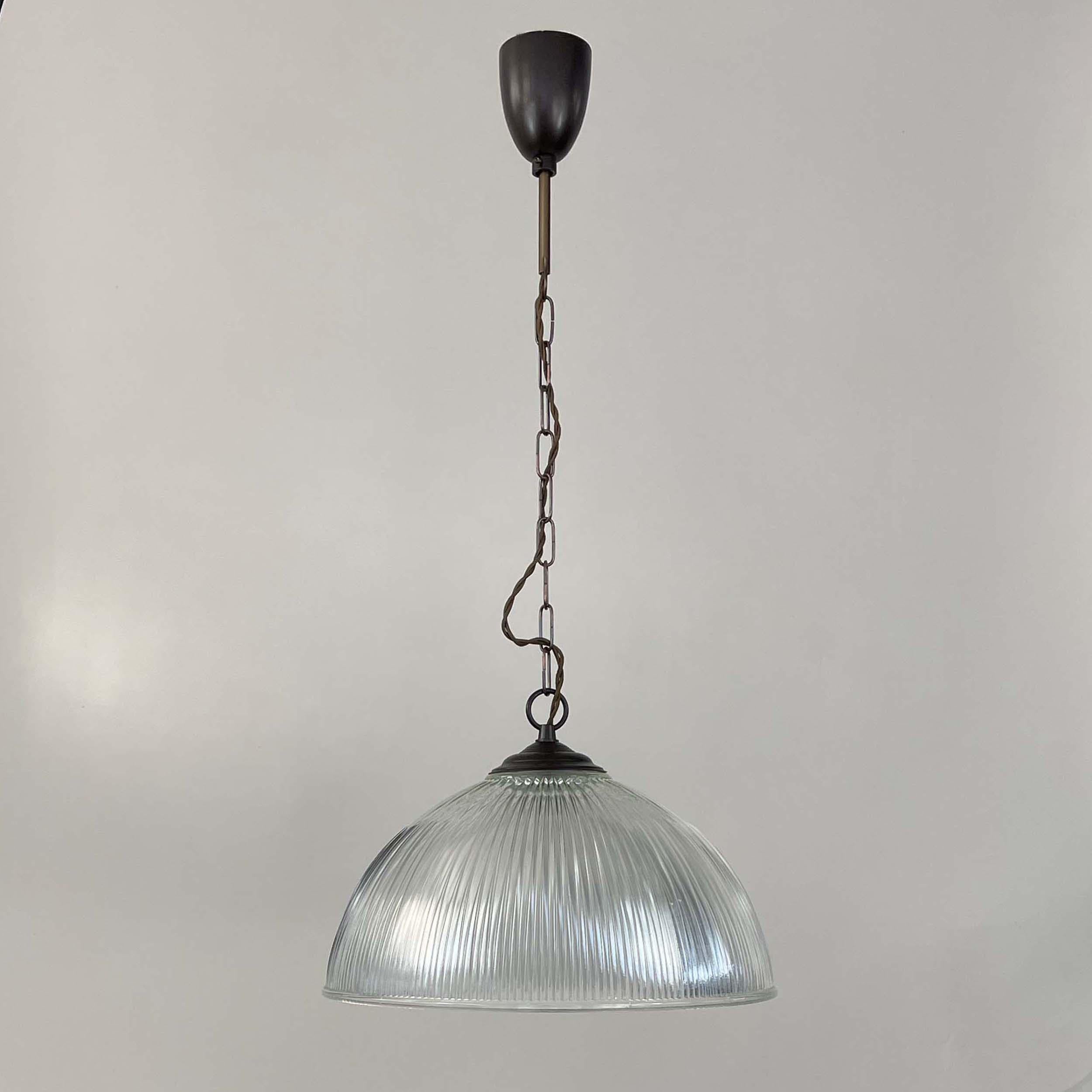 This industrial Art Deco dome shaped pendant light was manufactured in France in the 1930s. It features a clear prismatic glass Holophane lamp shade and patinated brass glass holder, chain and canopy. Rather heavy quality.

The glass gives off the