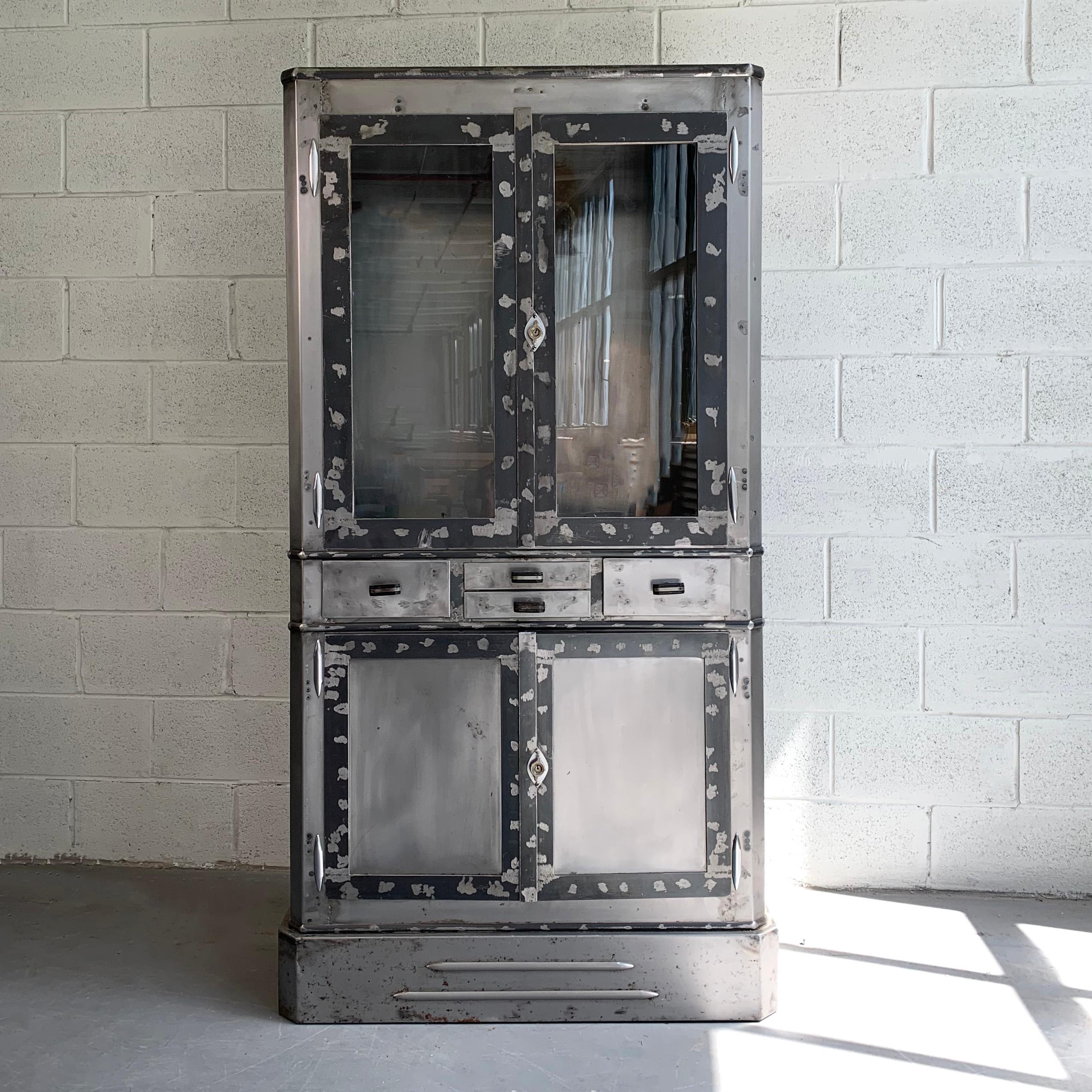 L'armoire d'apothicaire médicale Art déco présente une nouvelle finition en acier brossé à l'intérieur et à l'extérieur, avec une vitrine supérieure en verre et un tiroir fermé avec des poignées en bakélite. La taille réelle de l'armoire est de 34