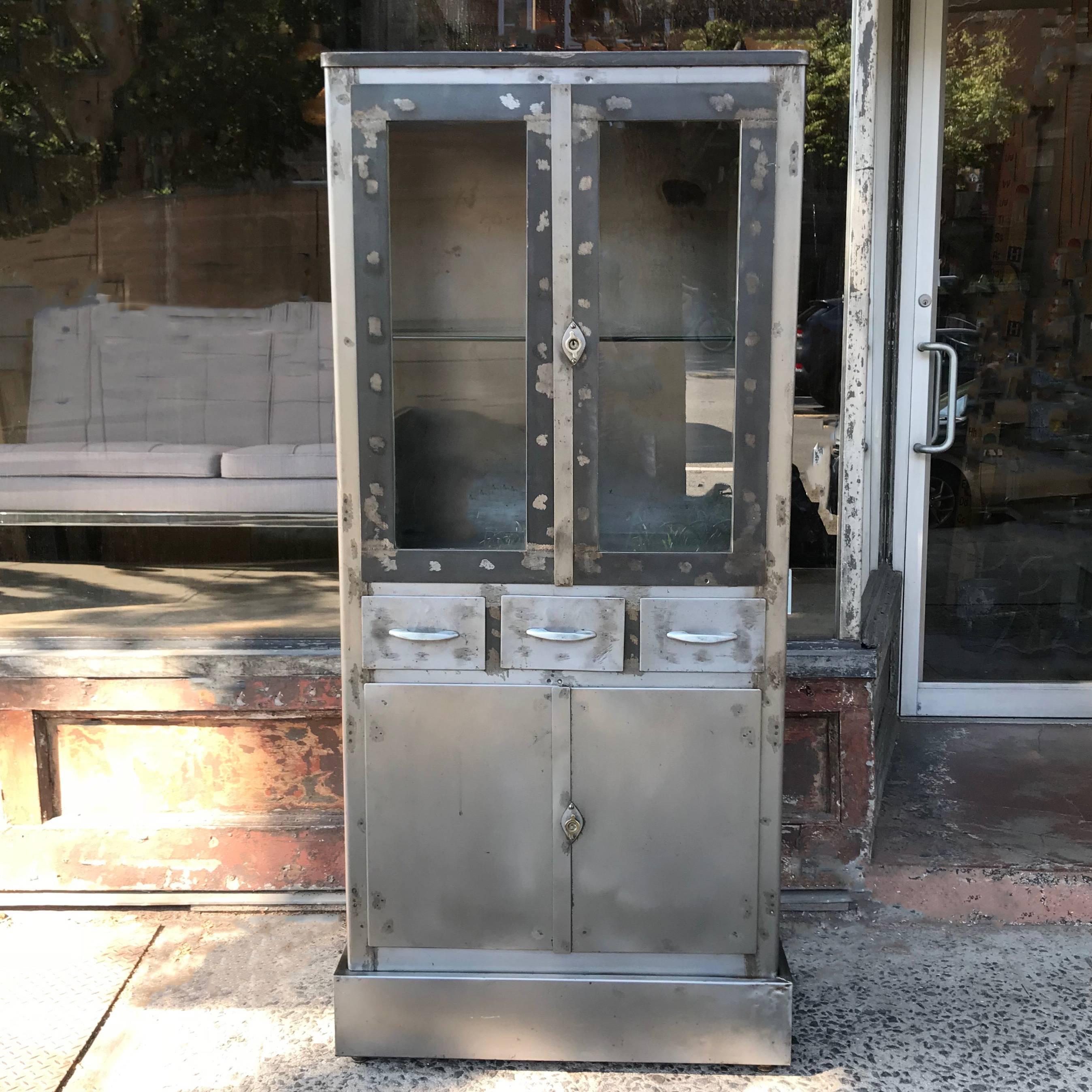 Art Deco, industrial, brushed steel, medical apothecary cabinet or vitrine features glass front display on top and closed storage on the bottom. The cabinet body measures 36 inches wide x 15 inches deep.