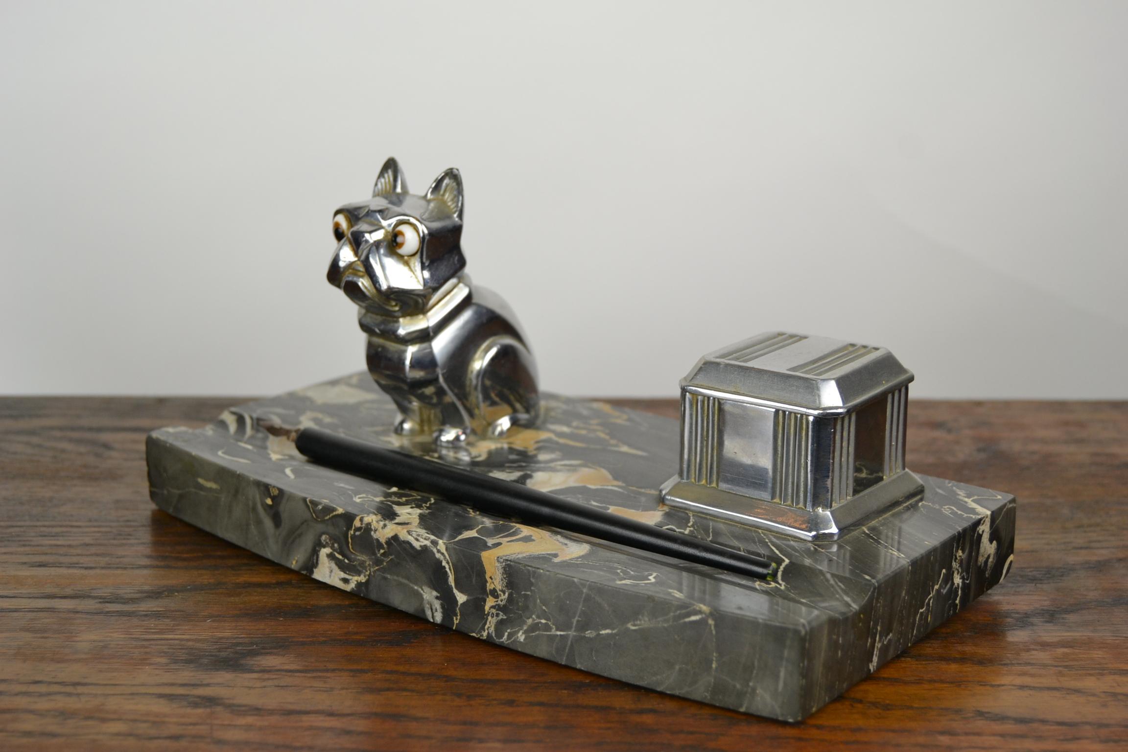 Stylish 1920s Desk Ornament, 
an Inkwell with a Chromed Cubist French Bulldog Figurine.  
The dog has bulging Brown Glass Eyes and is mounted on a black, grey and brown veined Marble Base , with also a chromed inkpot.

Bulldog is Signed : H. Moreau
