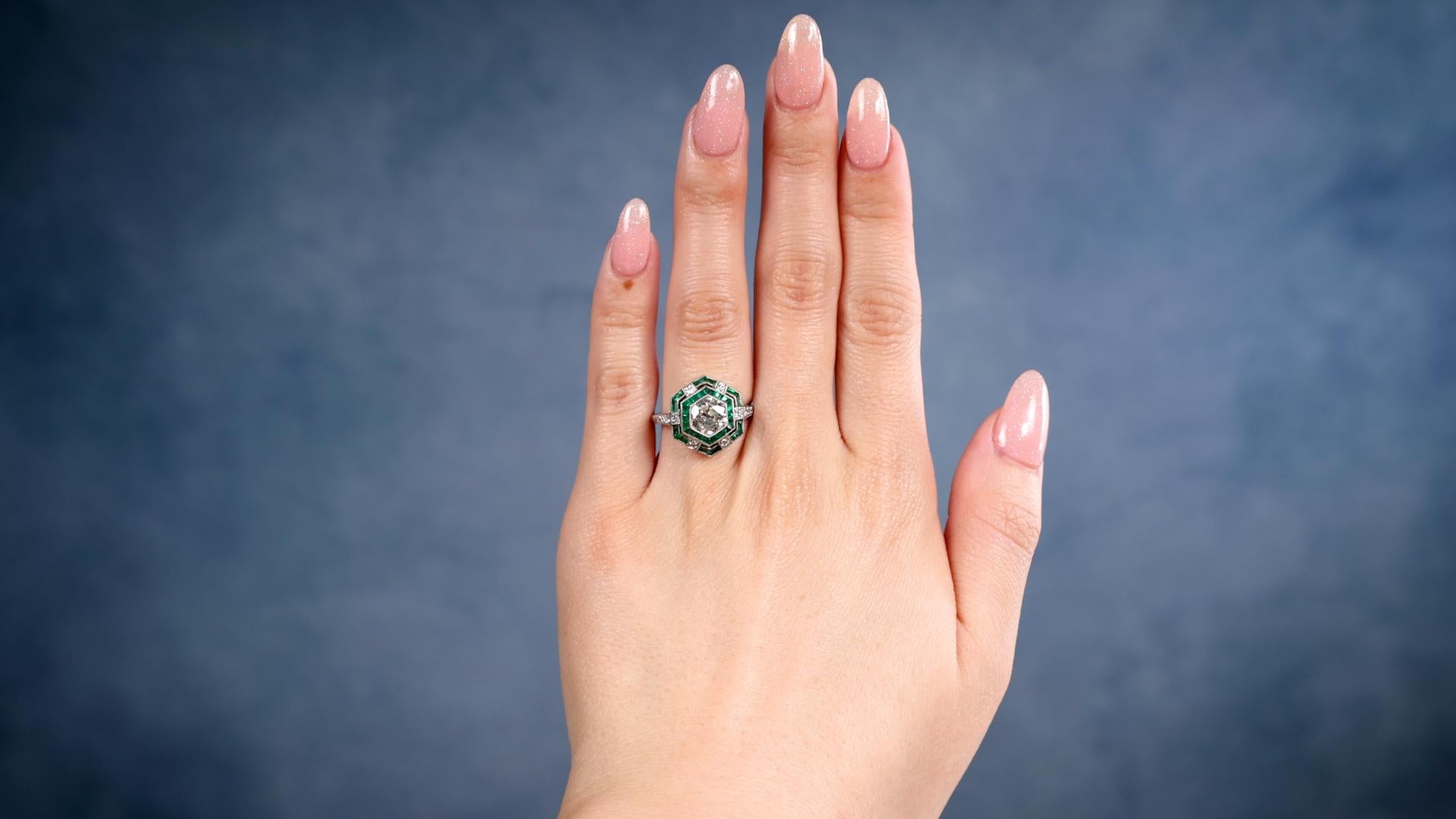 One Art Deco Inspired 1.00 Carat Old European Cut Diamond Emerald Platinum Ring. Featuring one old European cut diamond of 1.00 carat, graded K color, SI2 clarity. Accented by 30 calibré cut emeralds with a total weight of approximately 0.80 carat,