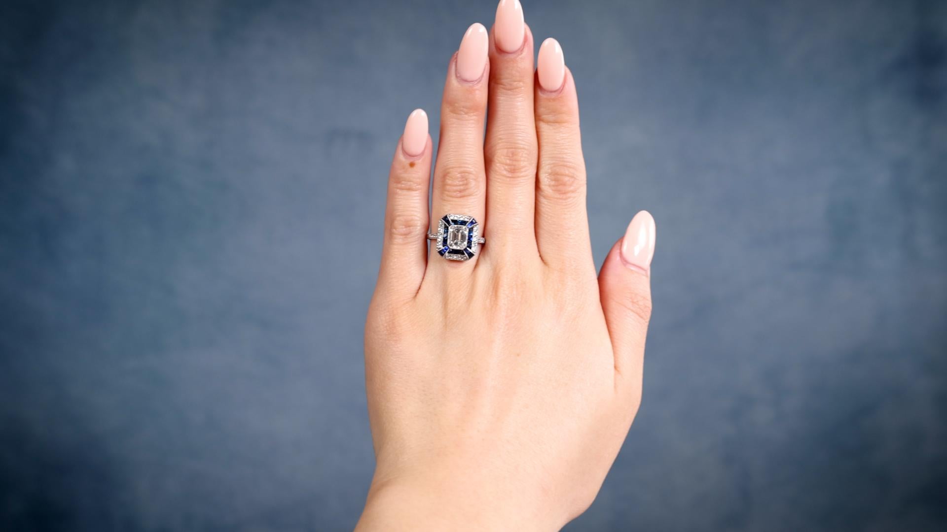 One Art Deco Inspired 1.06 Carat Emerald Cut Diamond Sapphire Platinum Ring. Featuring one emerald cut diamond of 1.06 carats, graded F color, VS1 clarity. Accented by 18 French cut sapphires with a total weight of approximately 1.20 carats, and 24