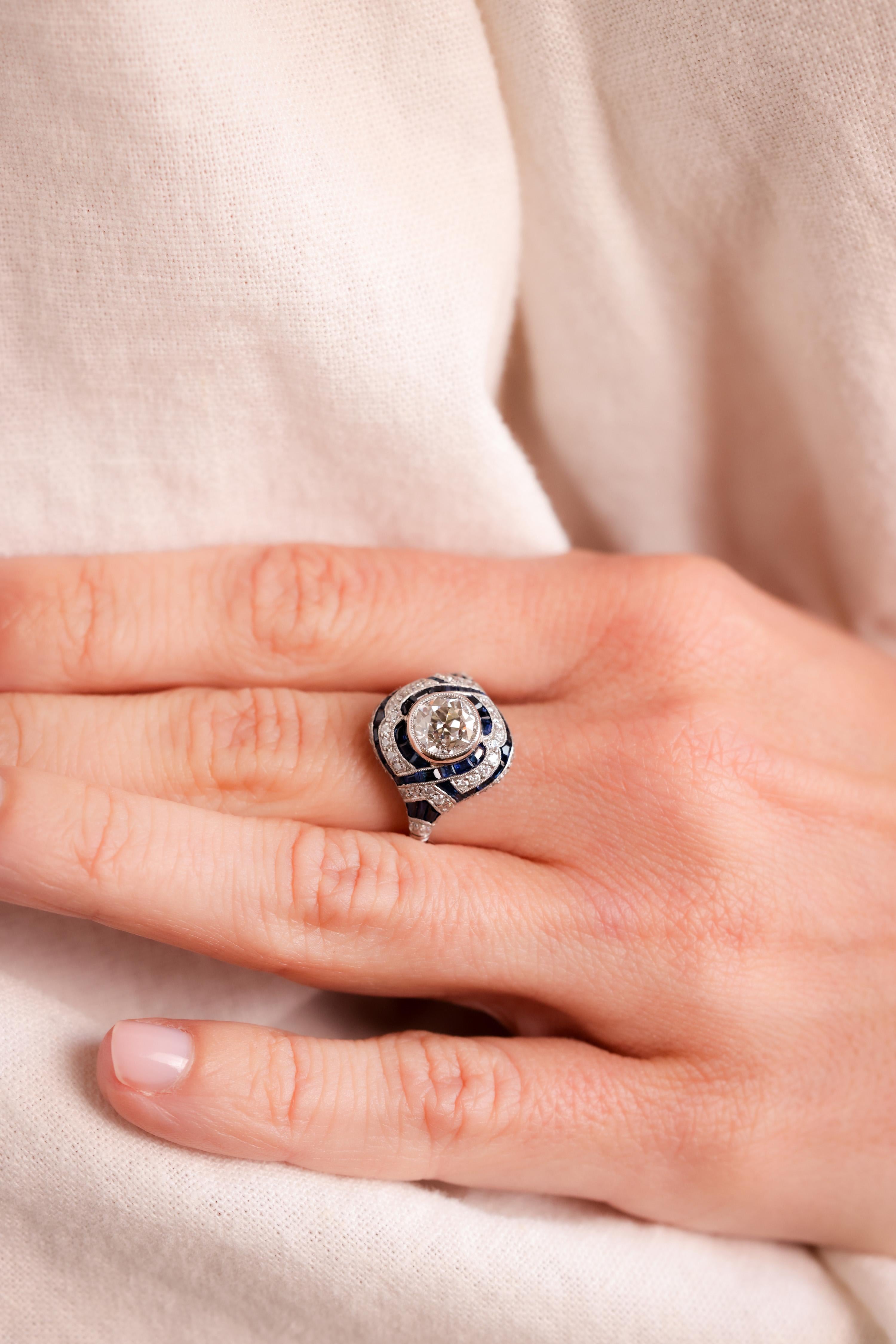 Center Stone: Diamond
Cut: Old European Cut
Weight: 1.22 Carat
Color: J-K
Clarity: VS2
Accent Stone: 43 Sapphires
Cut: Trapezoid, Baguette and Calibre cuts
Weight: Approximately 2 Carats
Color: Blue
Accent Stone: 62 Diamonds
Cut: Old European